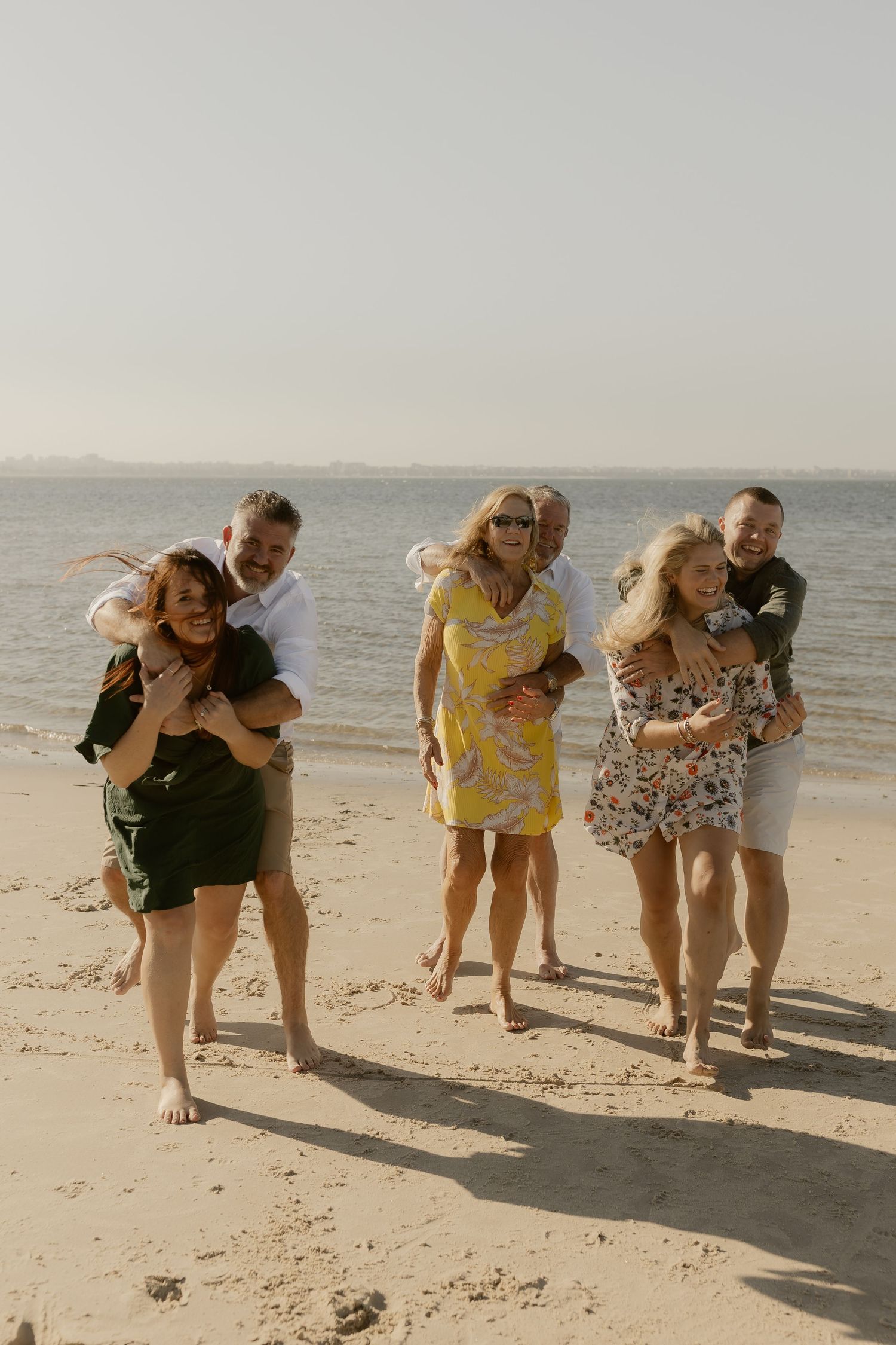 Candid beach photos showing a group having fun while bending down to look at something in the sand.