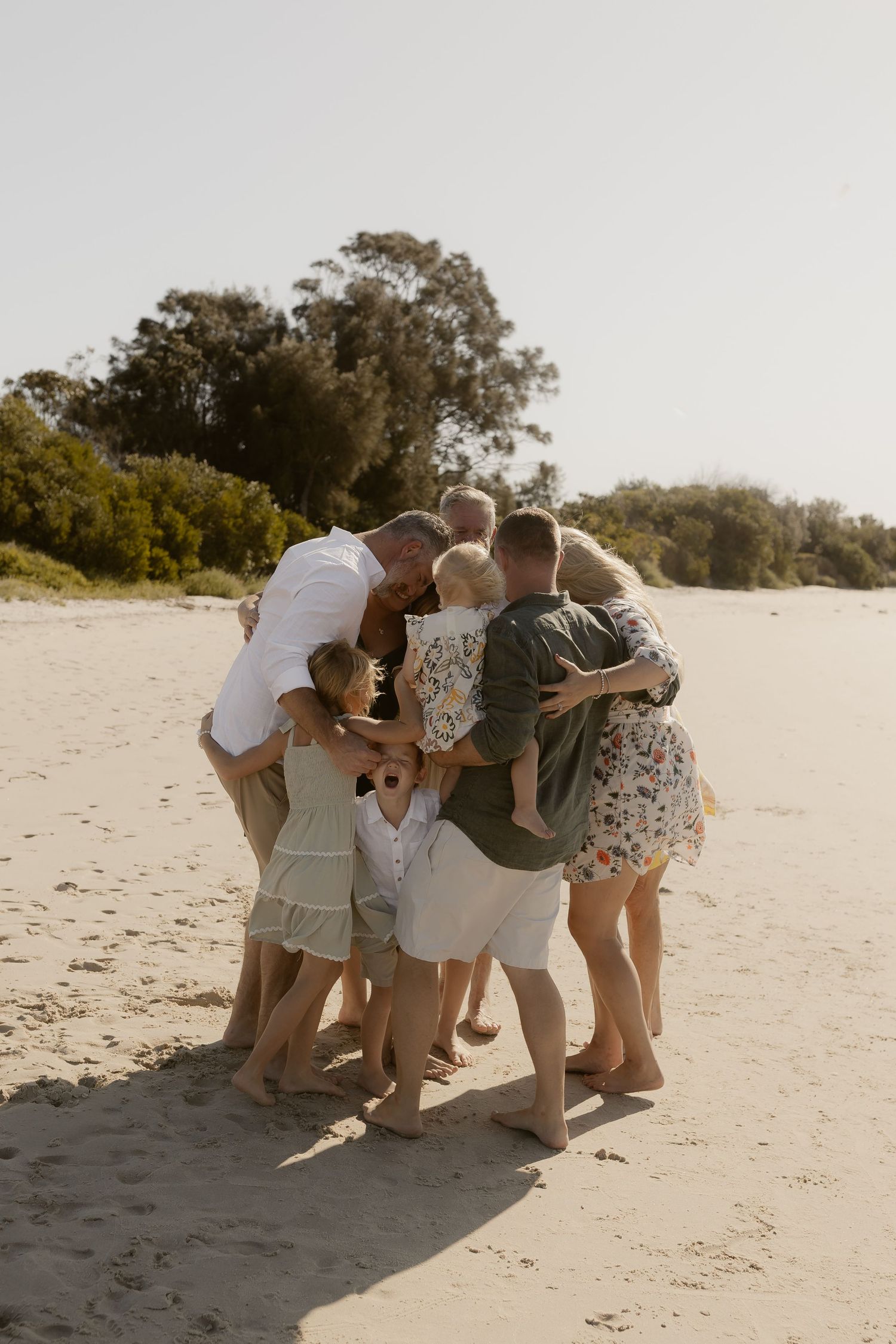 Group huddle on a sandy beach with people leaning in together against a bright sky.