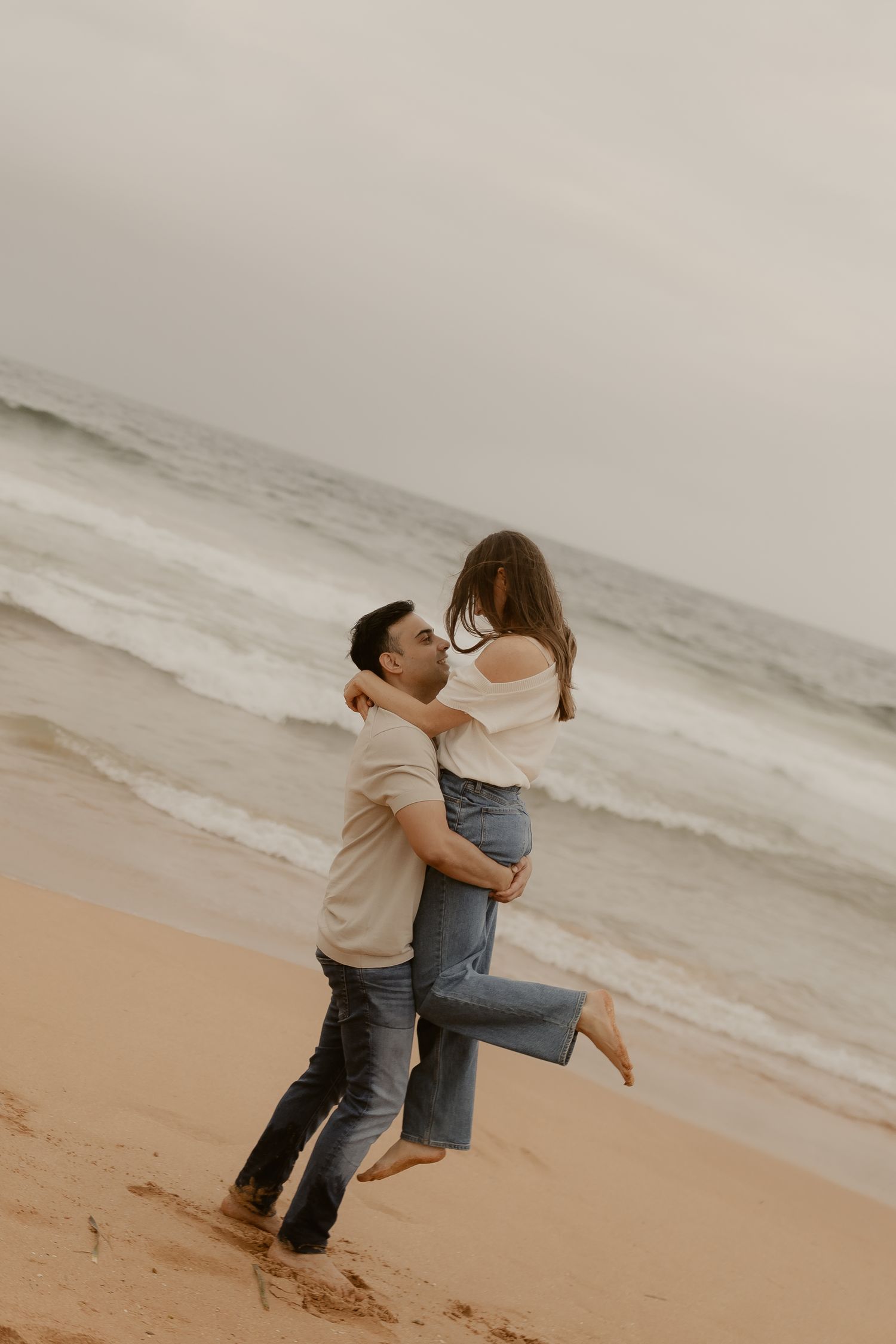 A romantic moment captured on a sandy beach with waves crashing in the background during golden hour.