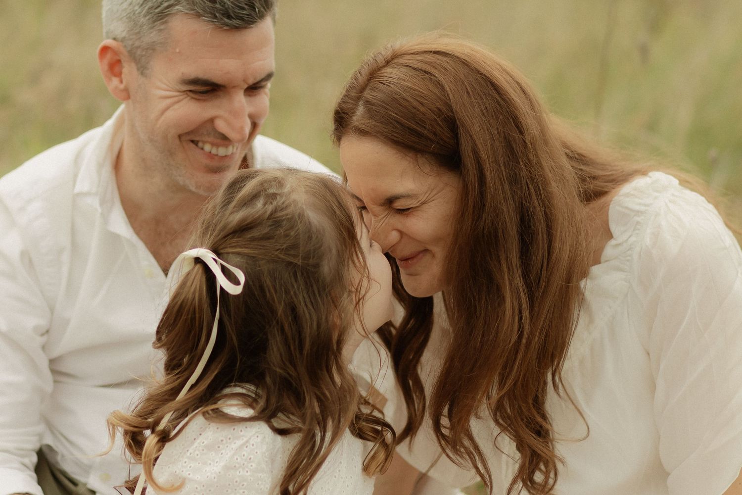 An intimate moment captured between loved ones in a field of tall grass during a photo session.