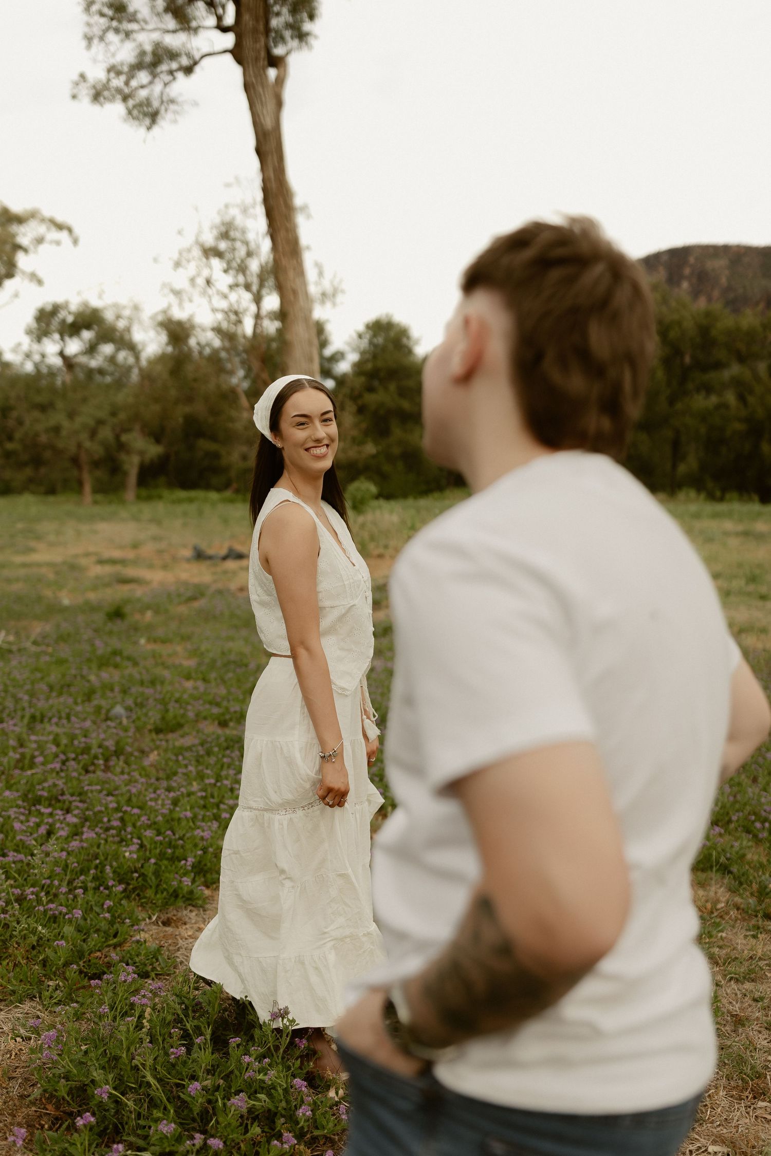 A couple dances and laughs together in a rustic outdoor setting at sunset.