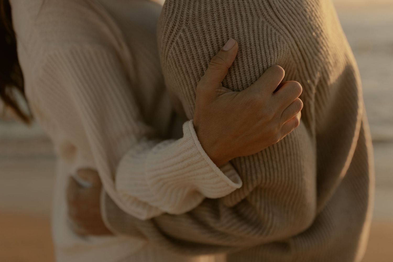 Close-up of couple in neutral sweaters sharing an intimate moment on the shoreline.