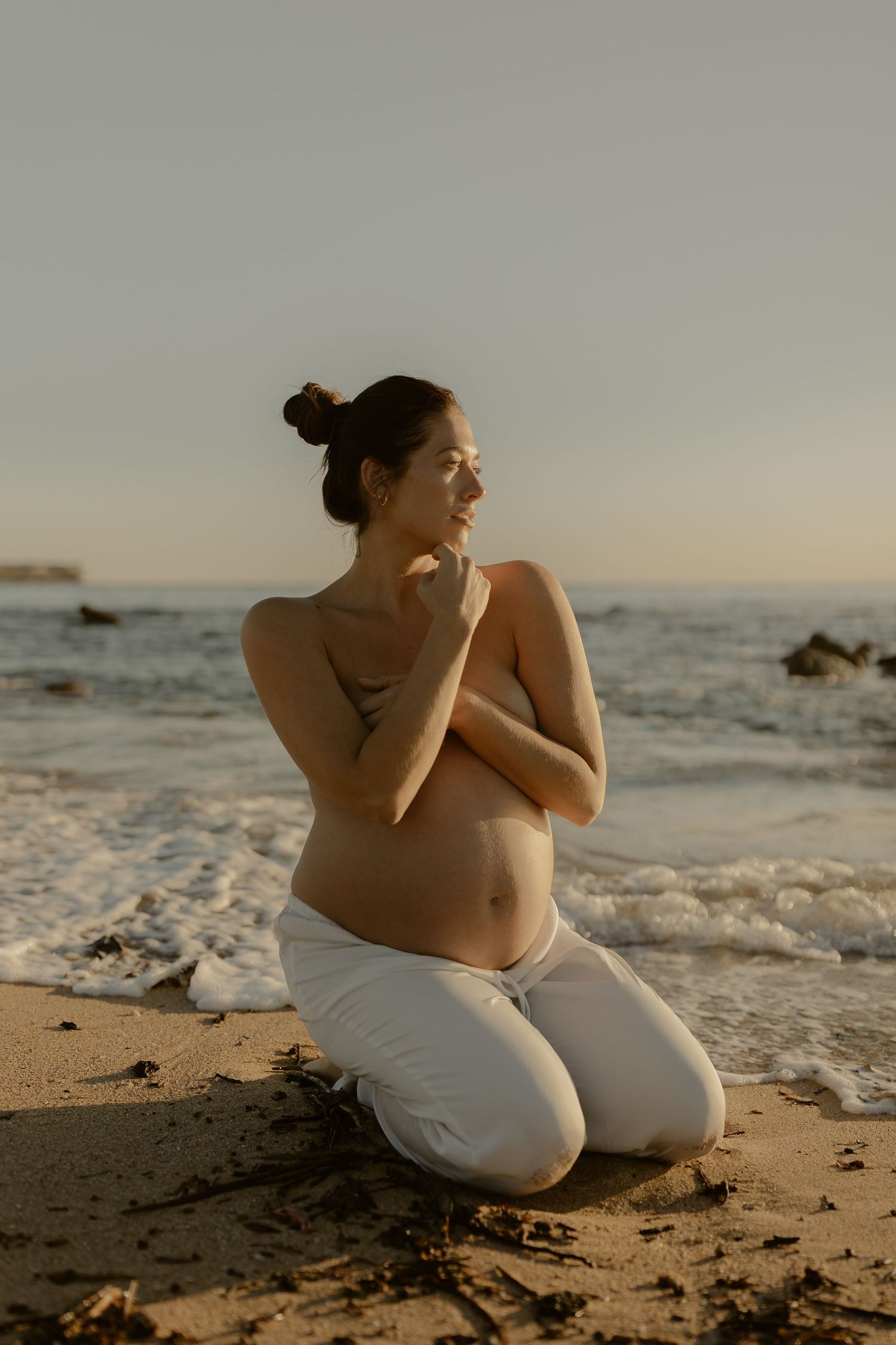 Maternity photo of woman kneeling on sandy beach at sunset.