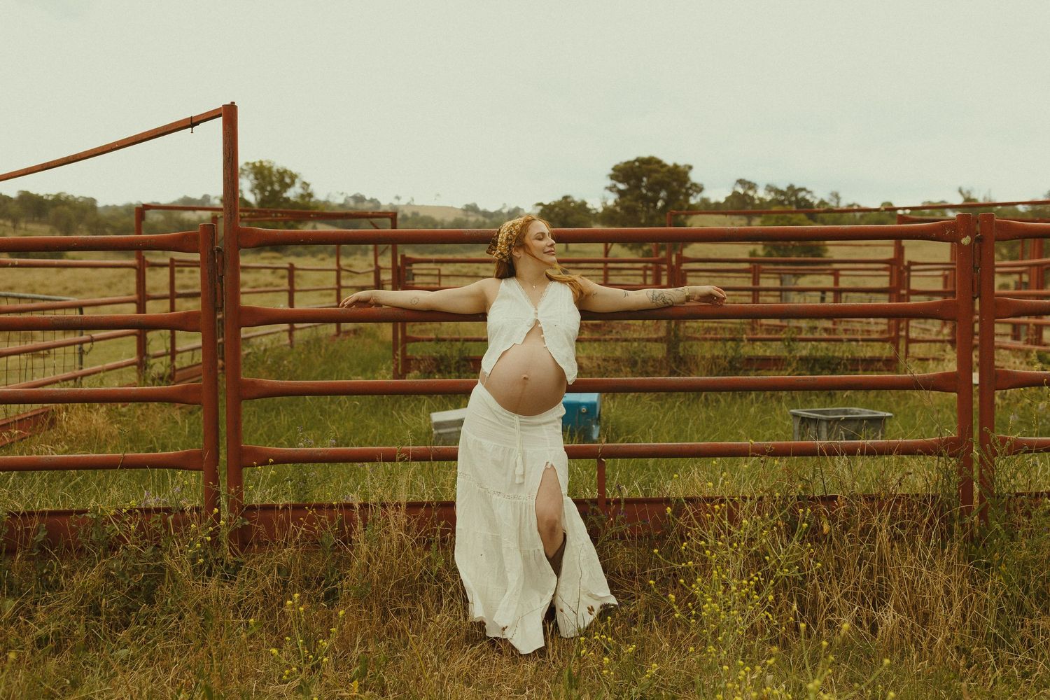 A rustic scene with wooden fencing and figures standing in tall grass during golden hour.