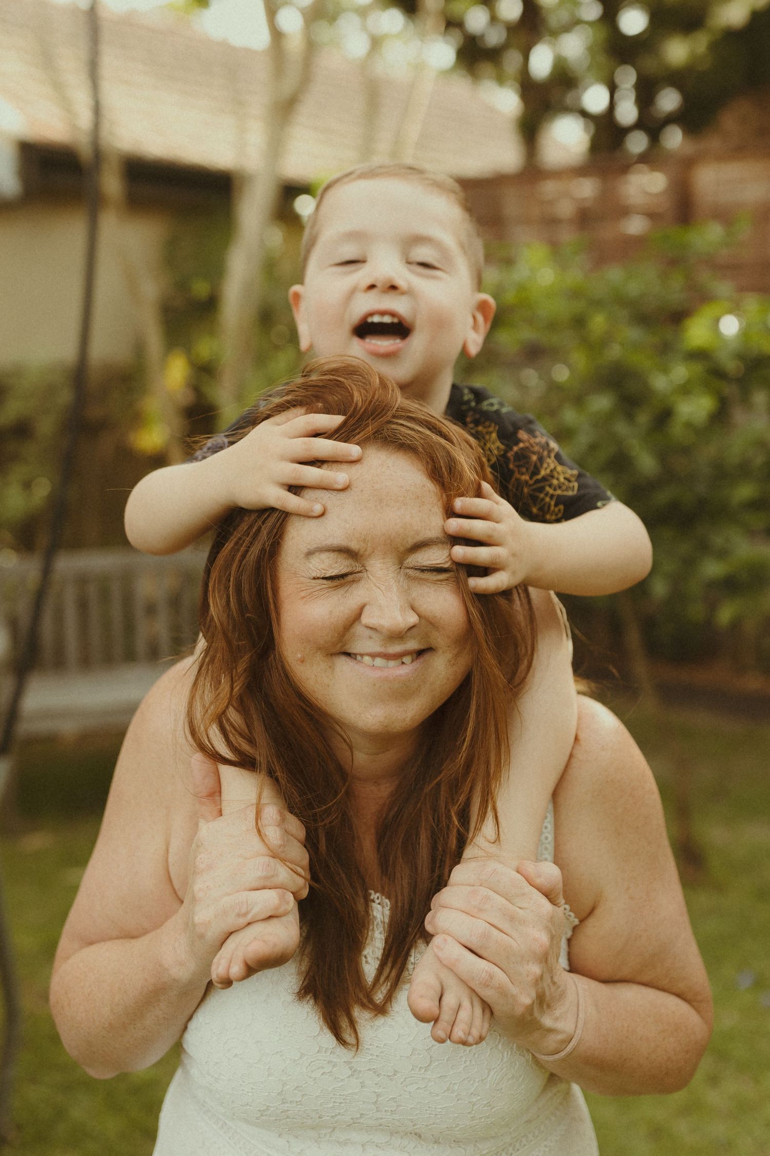 Playful family moment captured in a backyard with hands covering eyes and joyful expressions.