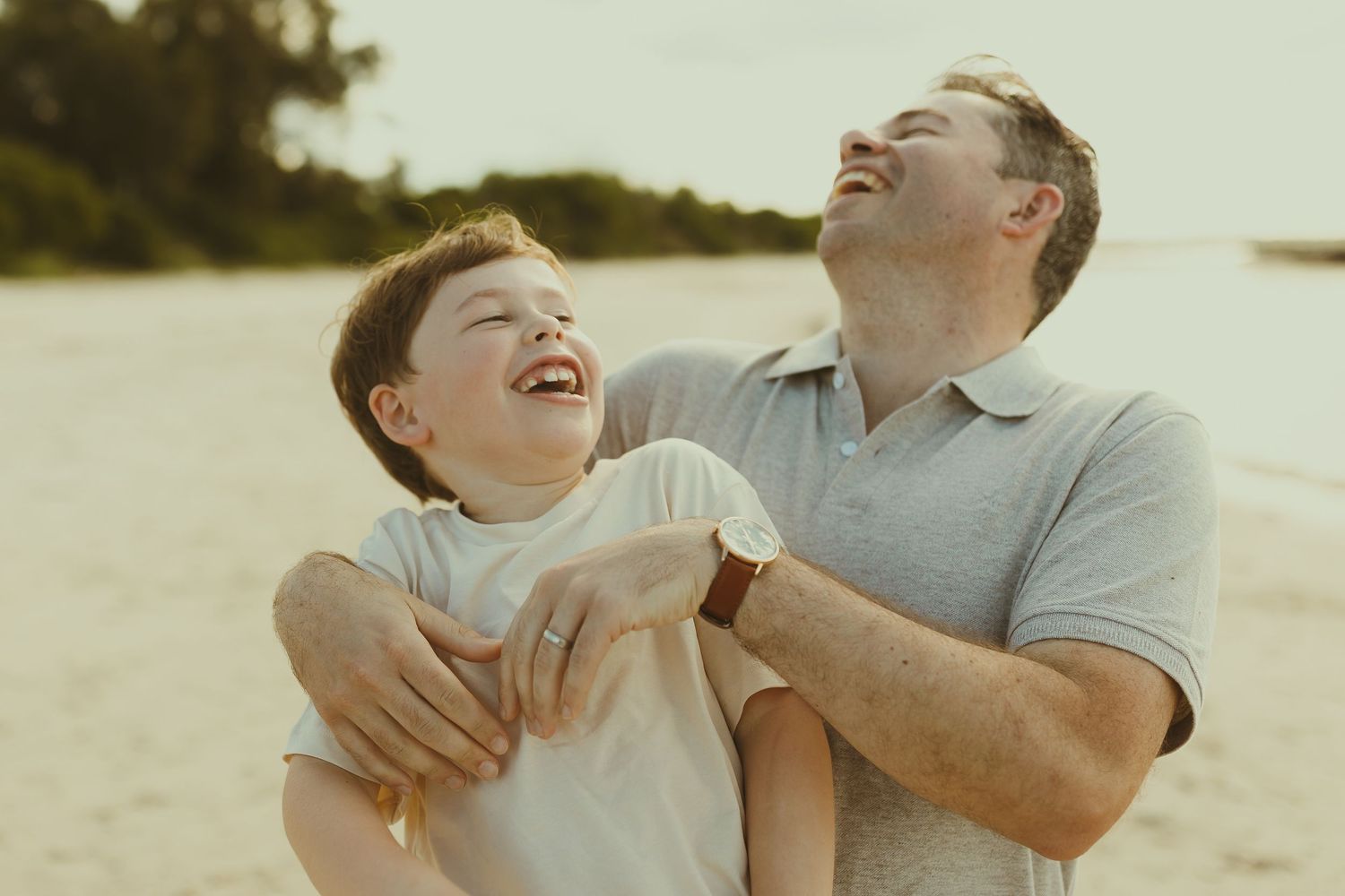 Candid laughter and embraces shared between family members on a sunlit beach.