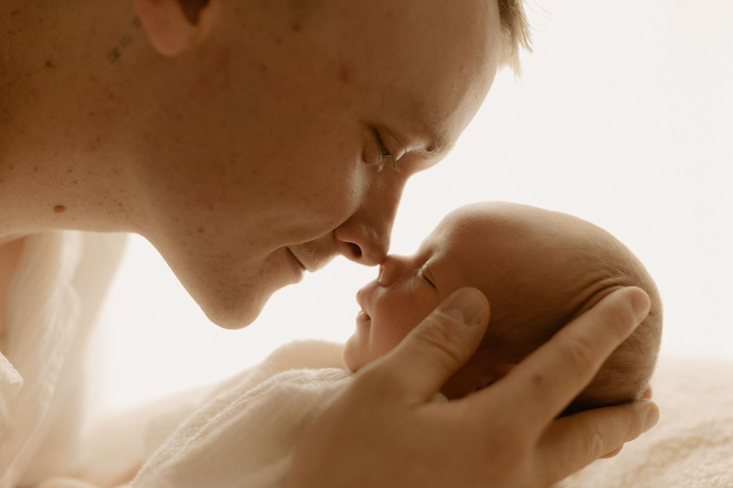 Sepia-toned intimate portrait capturing gentle moment between parent and newborn.