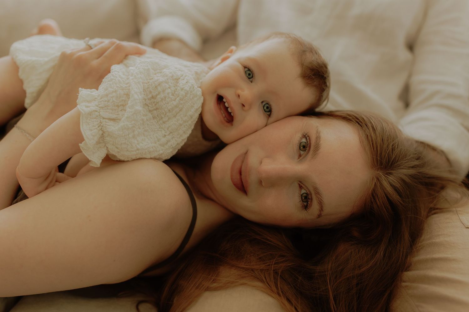 A young mother lying down with her smiling baby on her chest, sharing a tender moment together.