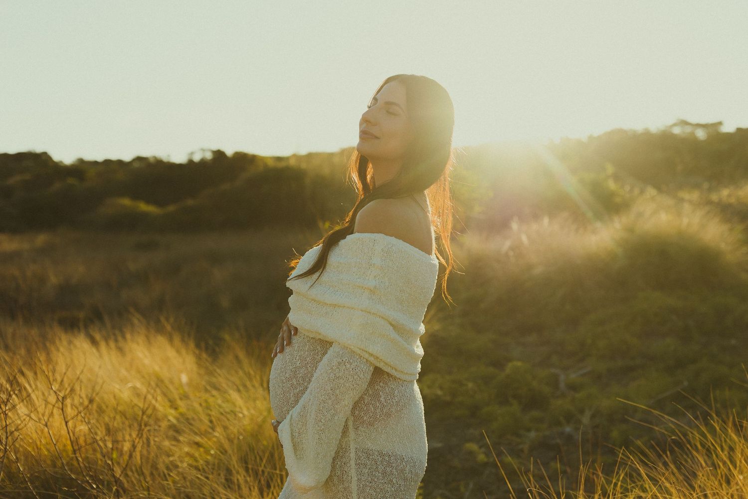 Silhouetted figure standing in golden sunlit field during sunset with backlit glow creating ethereal atmosphere.