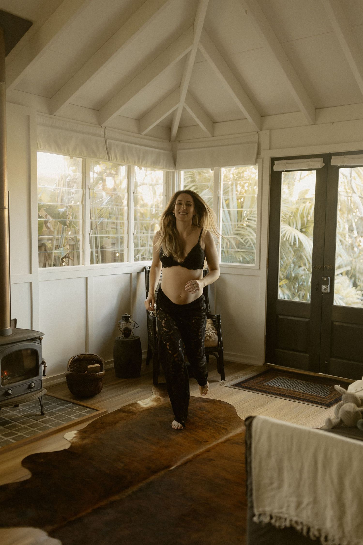A sunlit indoor space with a wooden floor, white walls, and a person standing in casual attire by a vintage stove.