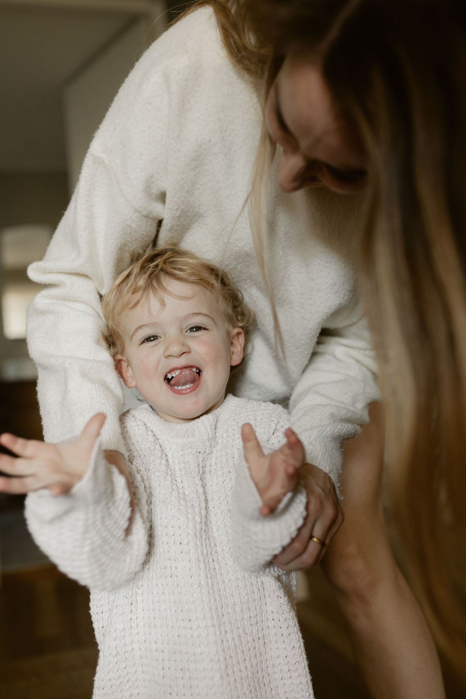 Joyful playtime moment in white knit sweaters with natural window lighting.
