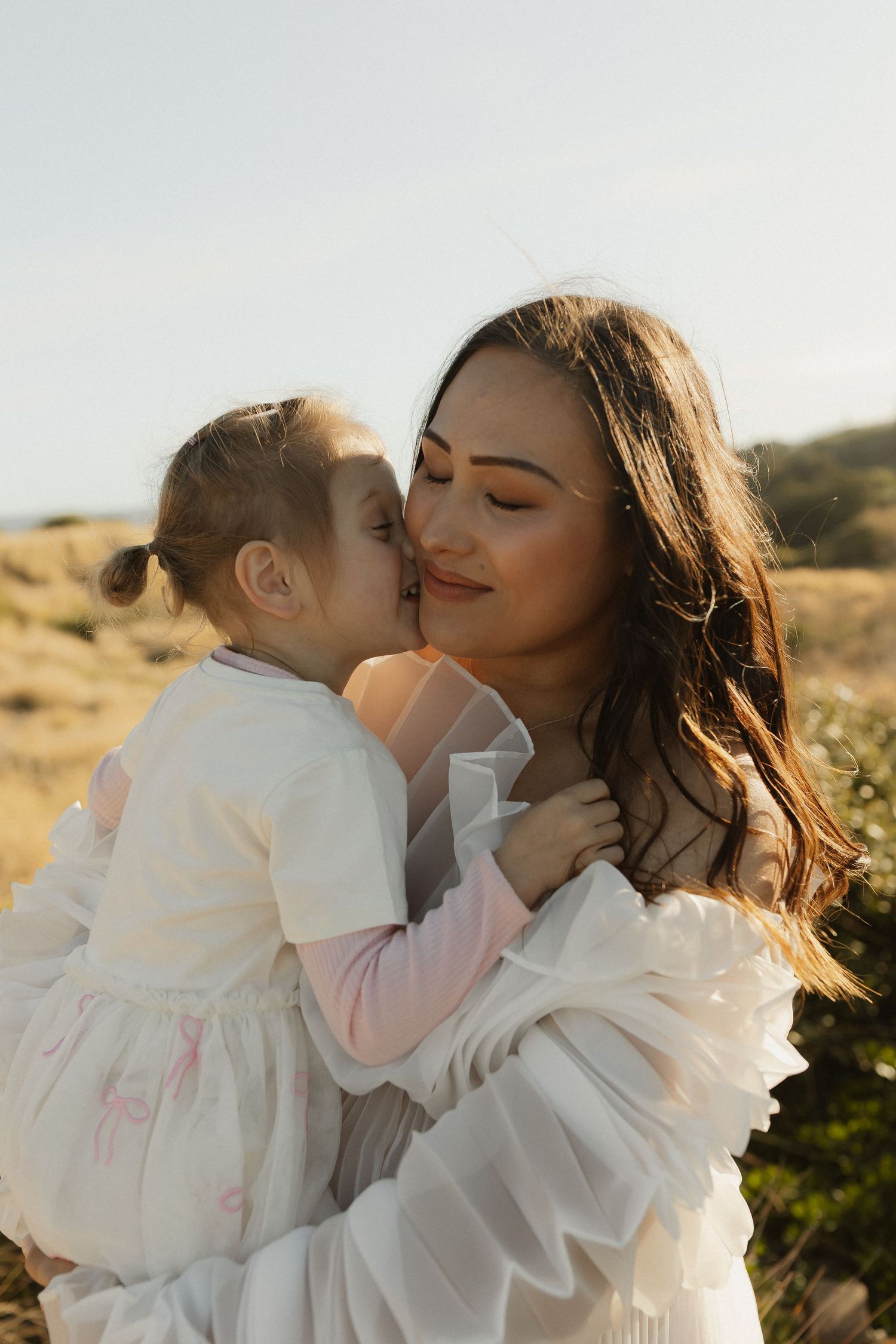 Sweet bonding moment between parent and child in white dresses at sunset.