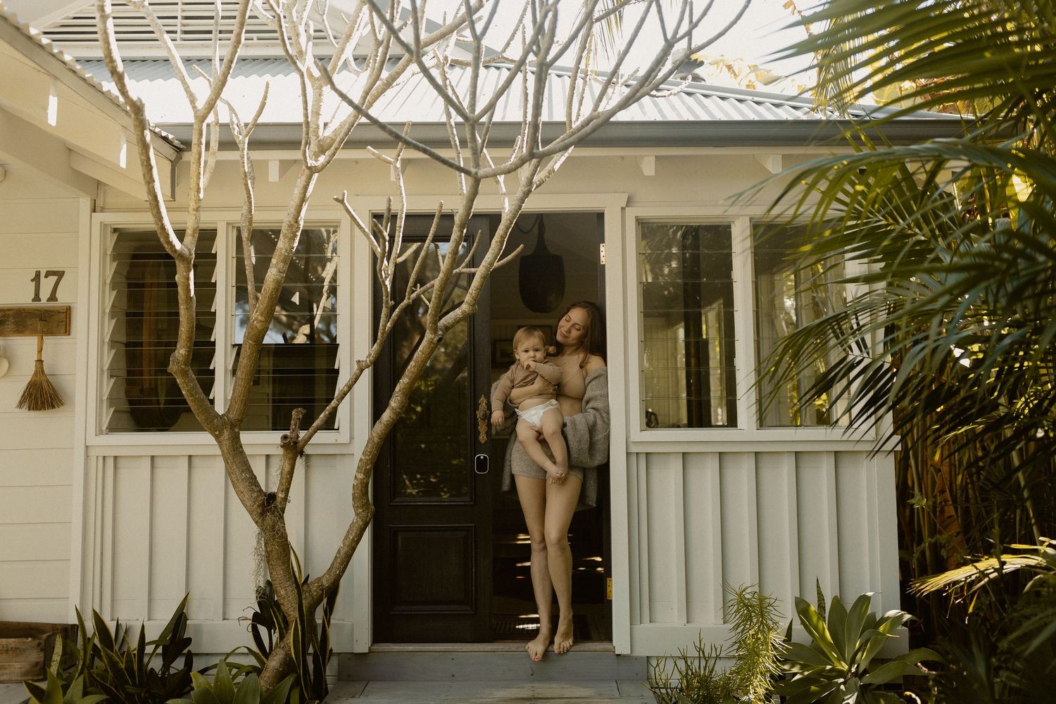 Sunlit porch scene with standing figures in light clothing against white house exterior.