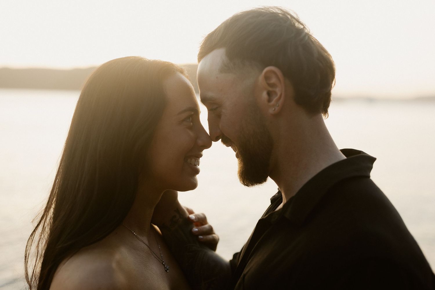 Intimate sunset silhouette portrait of a couple sharing a tender moment by the ocean.