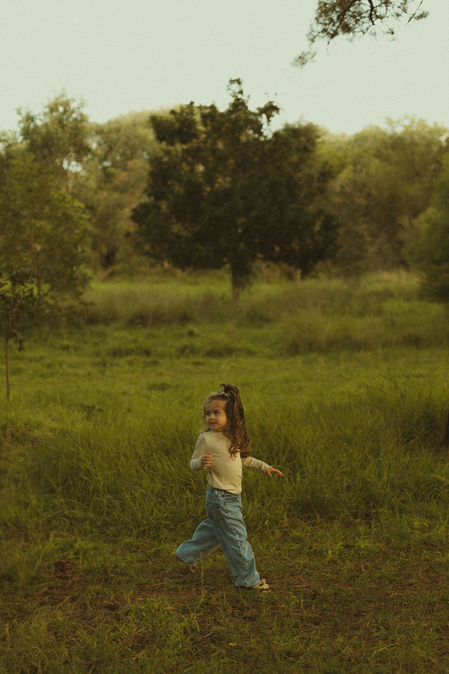 Young person walking through tall grass field at sunset with arms outstretched.