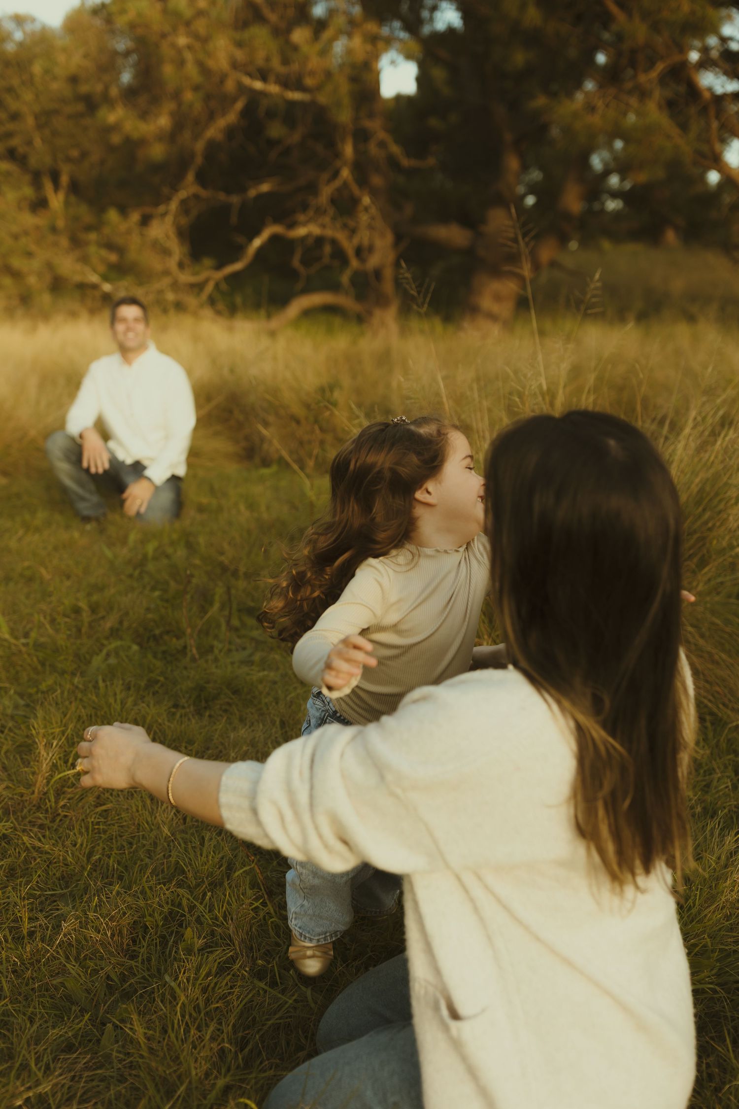 Family embraces in a sun-drenched field with golden grass and branches during sunset.