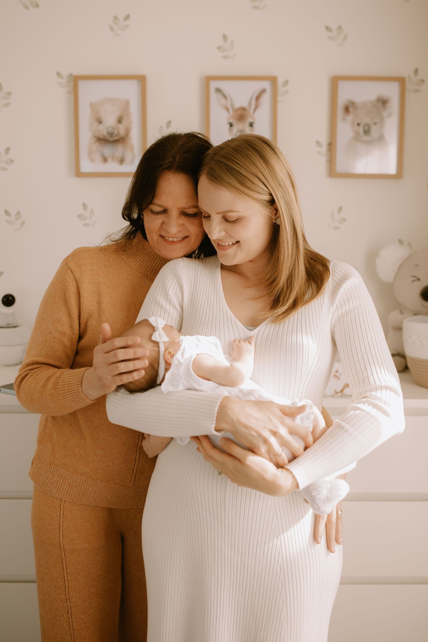 Two people sharing a tender moment while holding a newborn baby in a nursery with animal artwork on the wall.