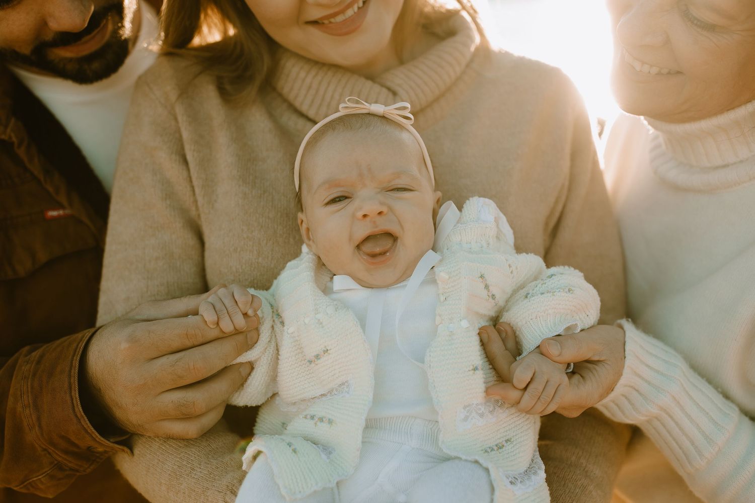 A smiling baby wearing white clothing photographed in warm sunlit tones.