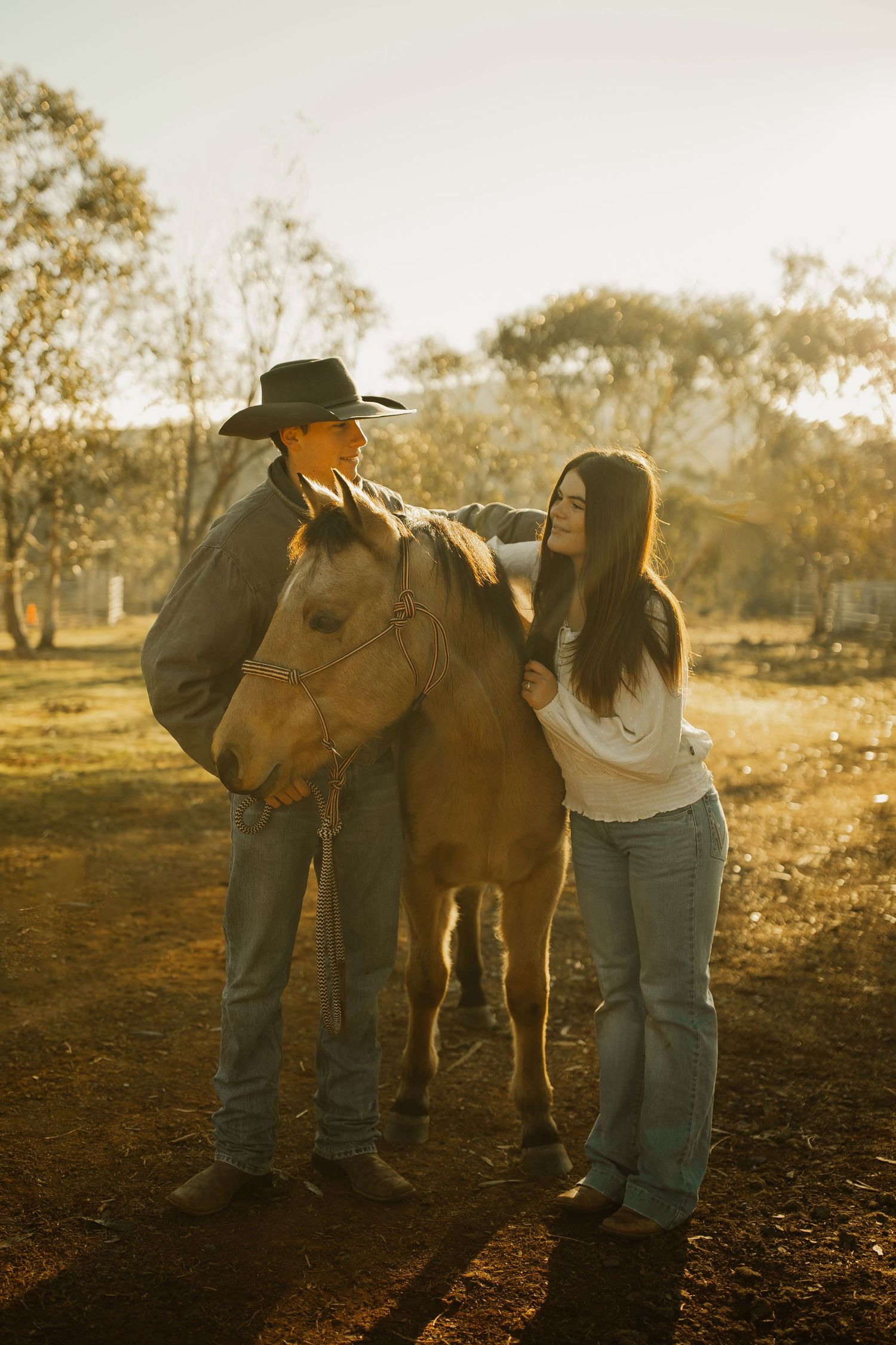 A couple with their horse at sunset in a rustic countryside setting with golden lighting.