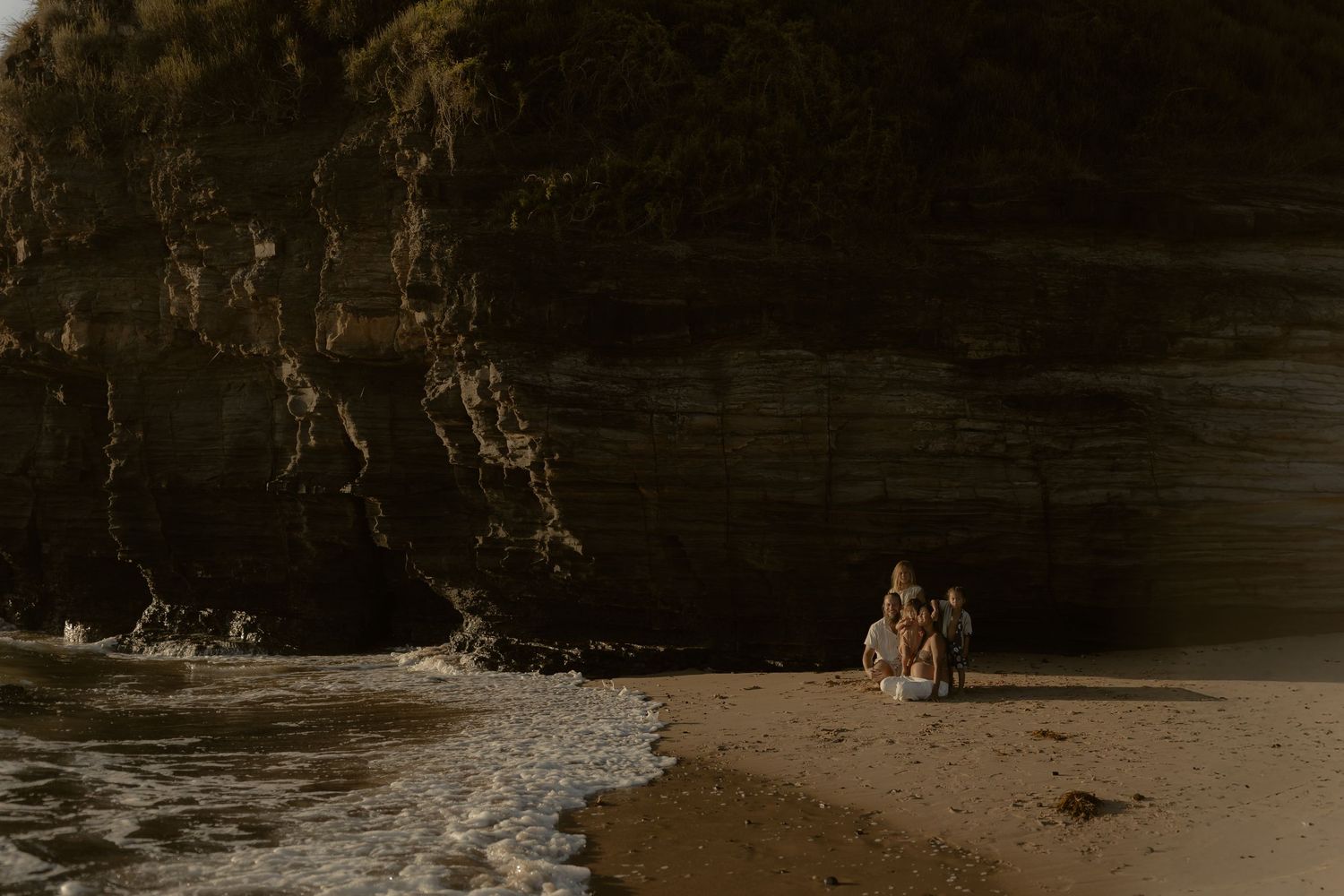 Couple walking along a dramatic rocky beach coastline at sunset creating silhouettes against the golden sky.