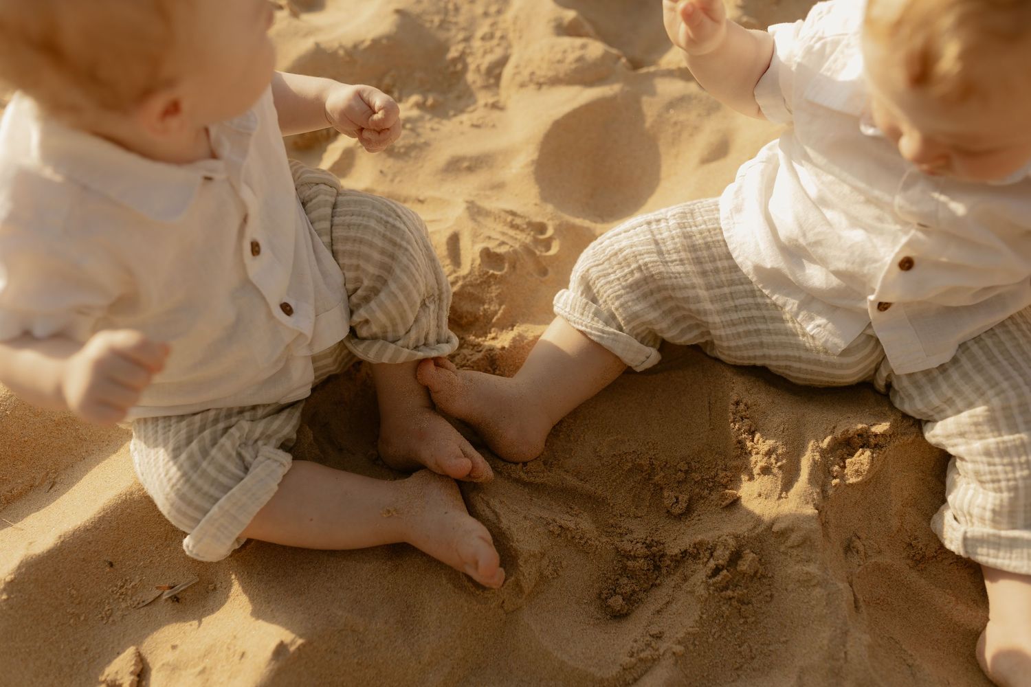 Small child plays in golden sand on a sunny beach, leaving handprints and footprints in the soft ground.