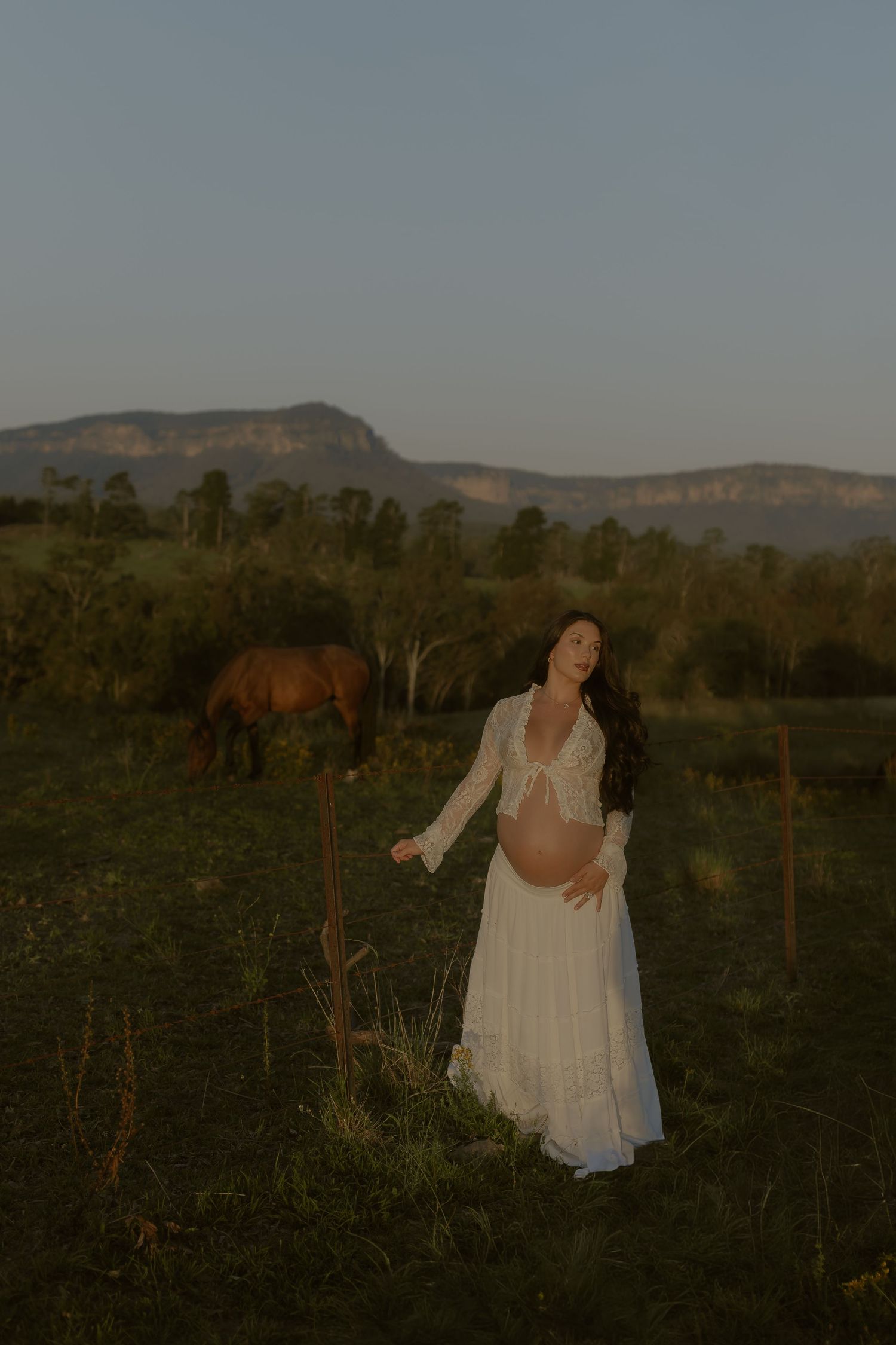 White-dressed figures move gracefully through a rustic field with mountains visible in the distance.