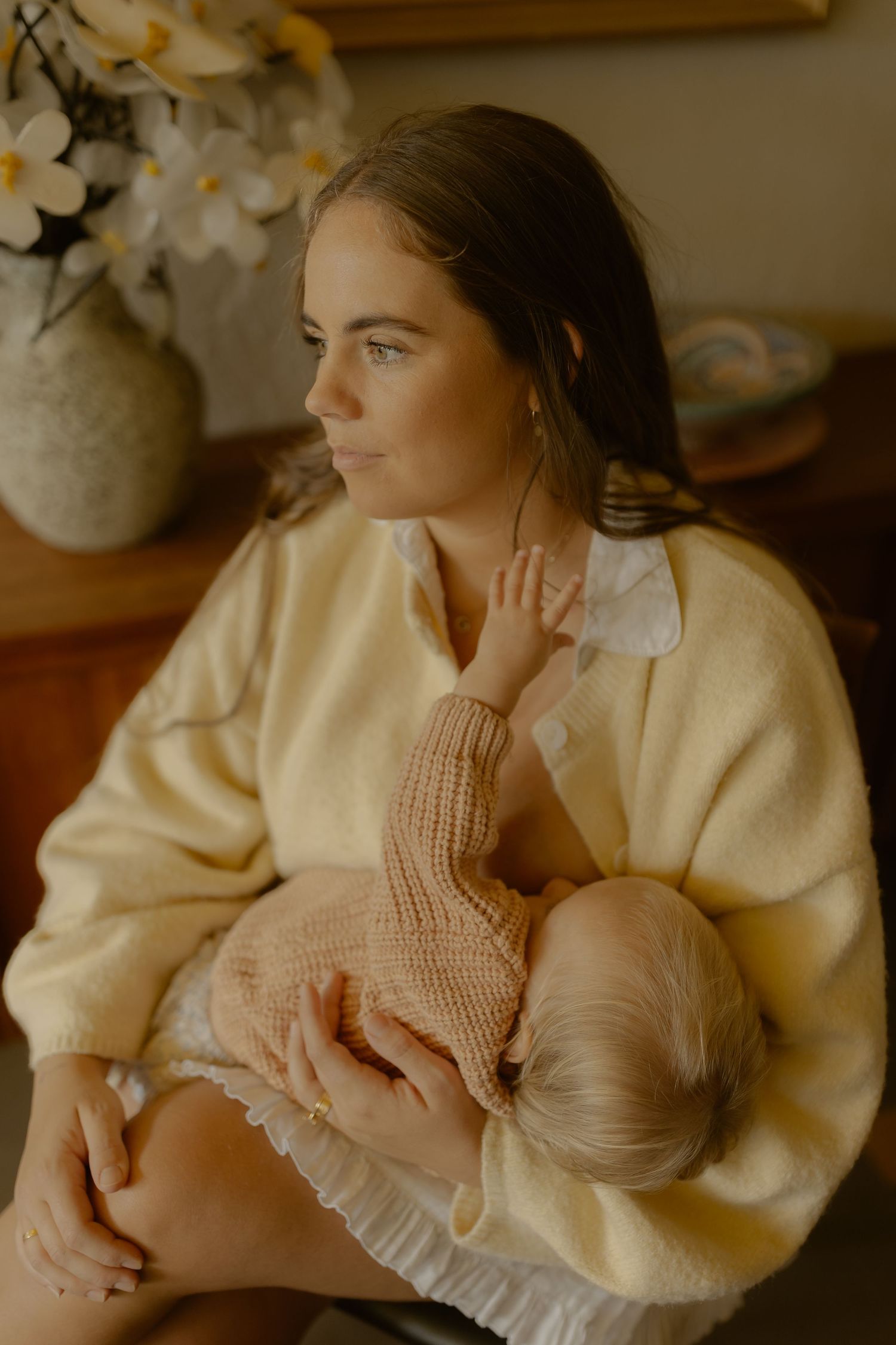 Close-up of mother in yellow sweater tenderly breastfeeding infant in soft natural light.