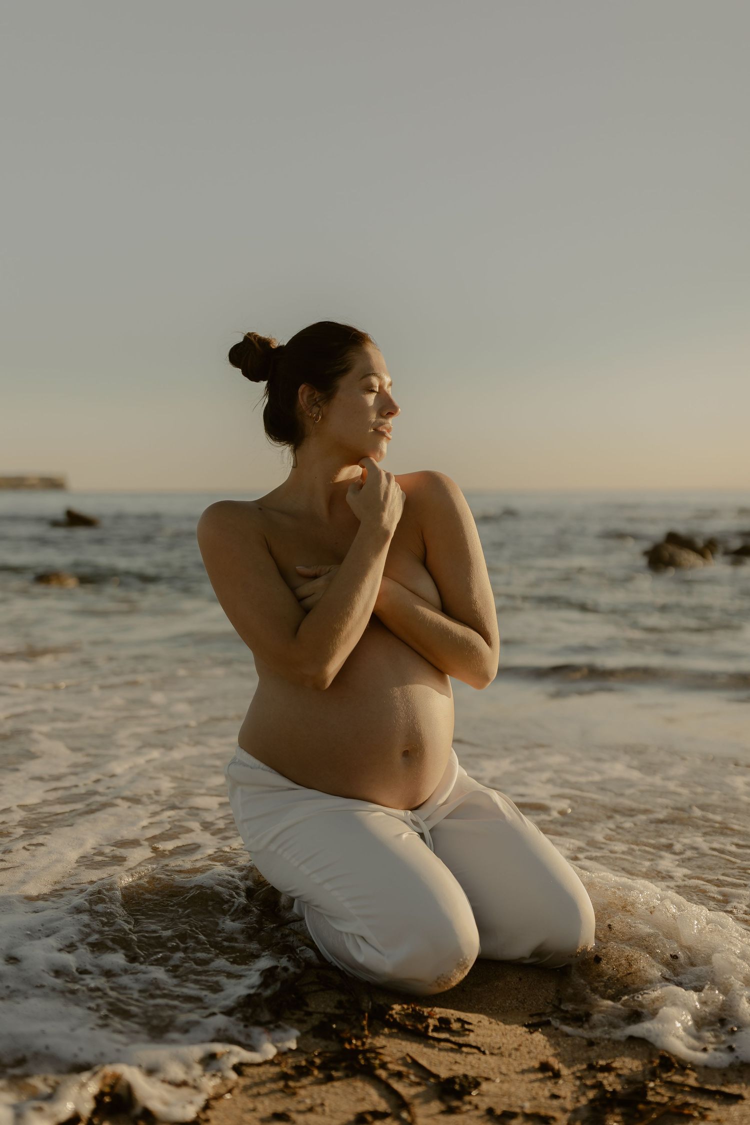 Sunset maternity photos at the beach showing silhouettes against ocean waves and golden light.