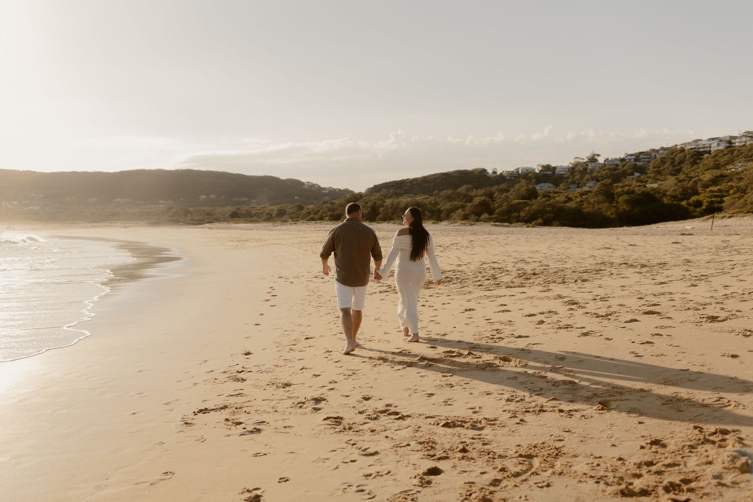 Panoramic view of a sandy beach with people walking along the shoreline at sunset.