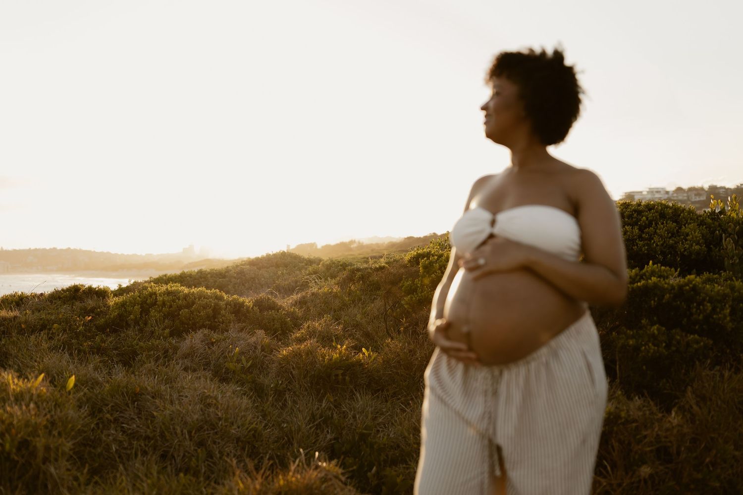 Silhouetted figures embrace during golden hour in a serene outdoor setting with rolling hills in the background.
