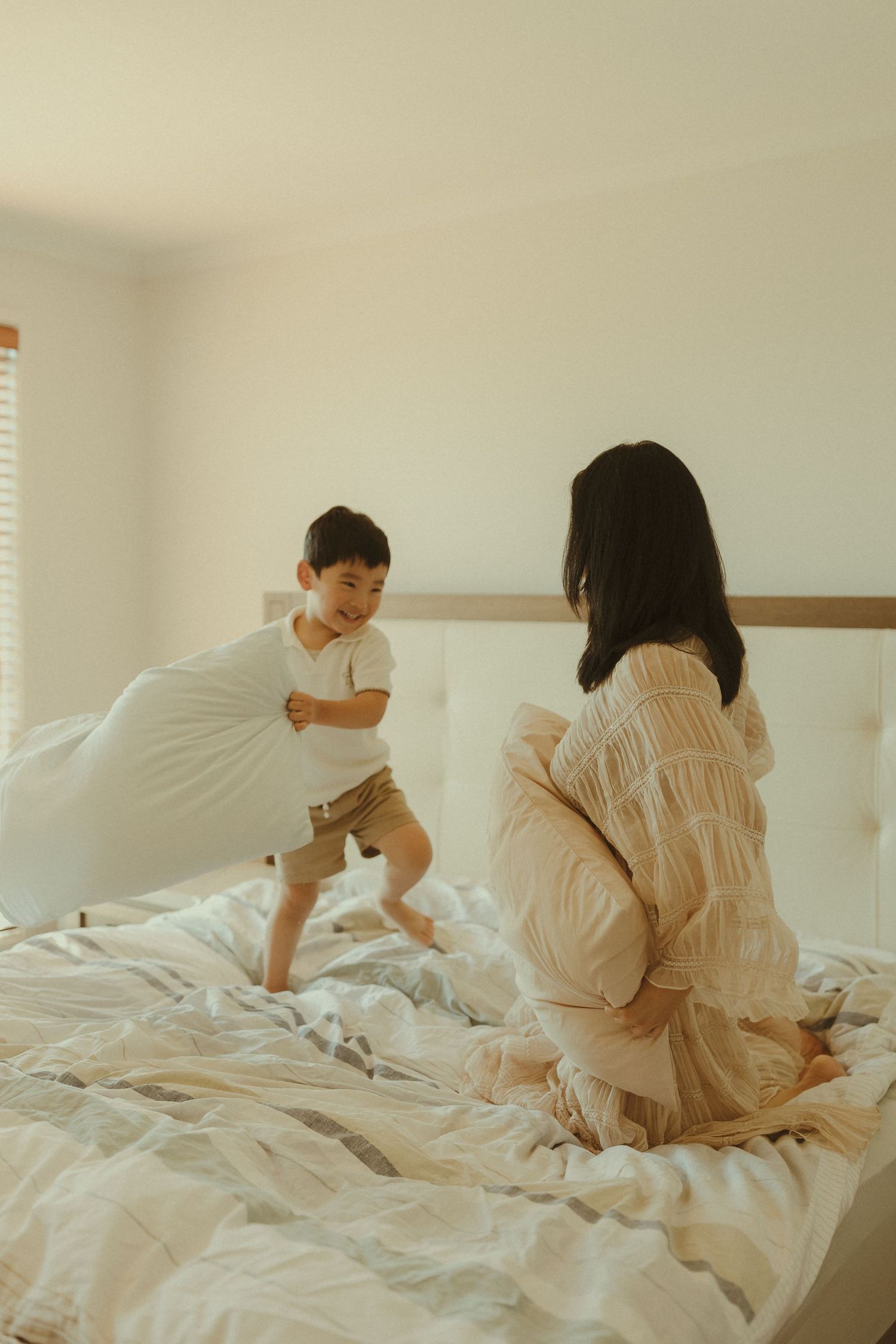 Family members playing and jumping together on a white unmade bed in a bright room.
