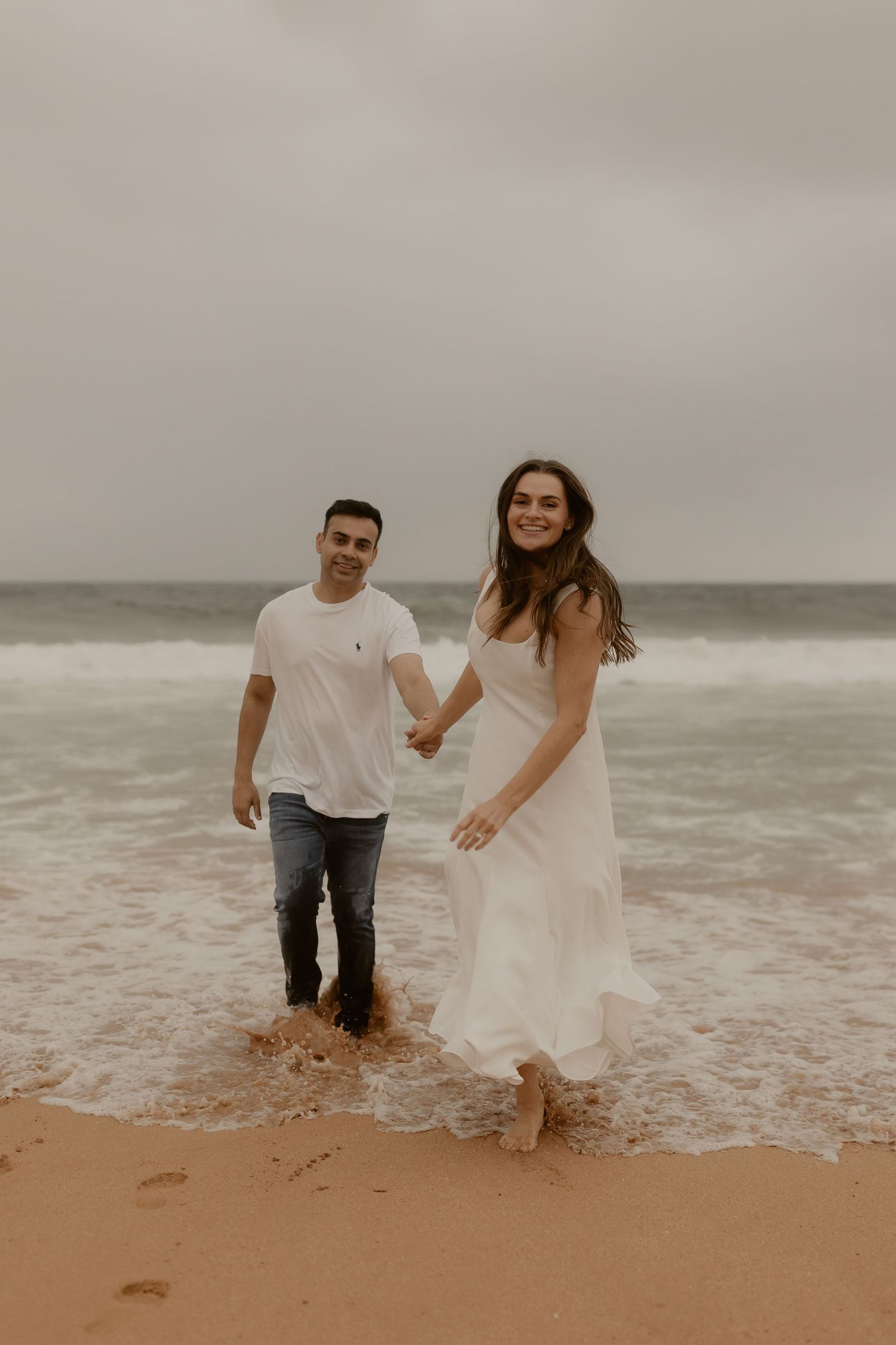 A couple splashes and plays in the shallow ocean waves at the beach's edge.