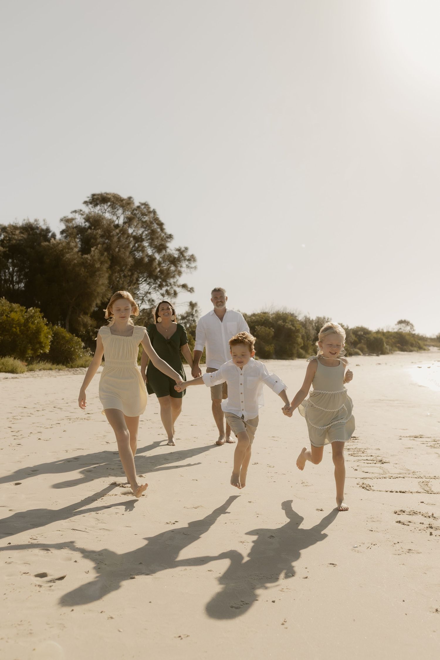Happy group running and playing together on a sunny beach with long shadows.