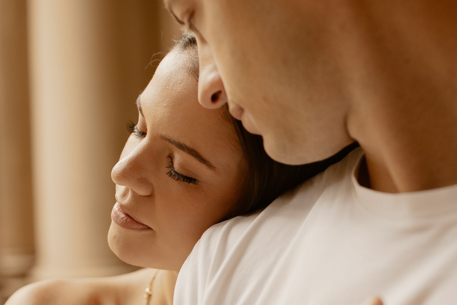 Intimate close-up portrait of a couple in soft warm light with closed eyes and peaceful expressions.