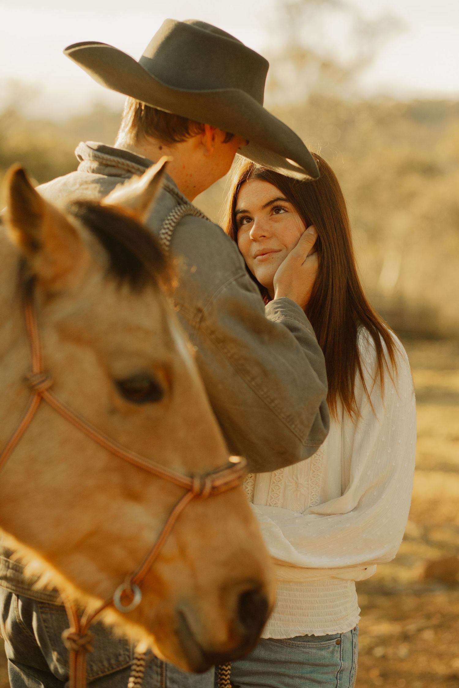 Romantic photo of a couple embracing in a warm sunset glow with a horse in the foreground creating a western country mood.