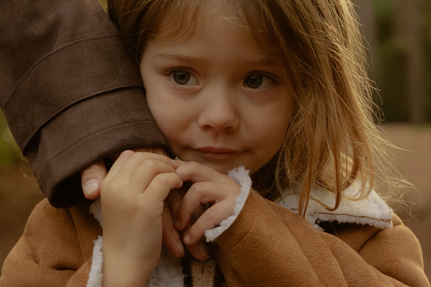 A young girl with blonde hair clutches a brown coat, looking sad and vulnerable in a touching emotional moment.