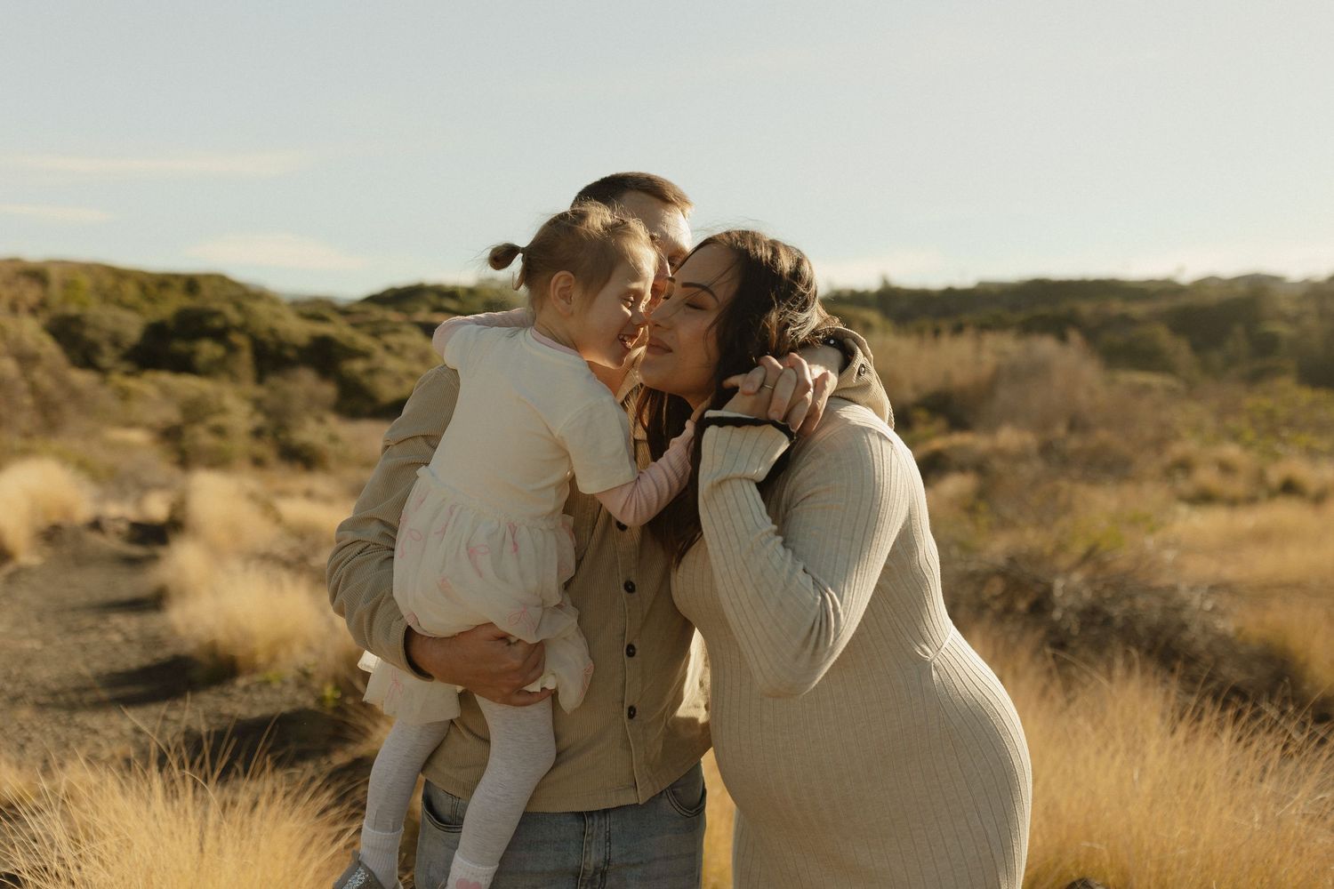 Tender family moment captured in warm evening light among tall grass.