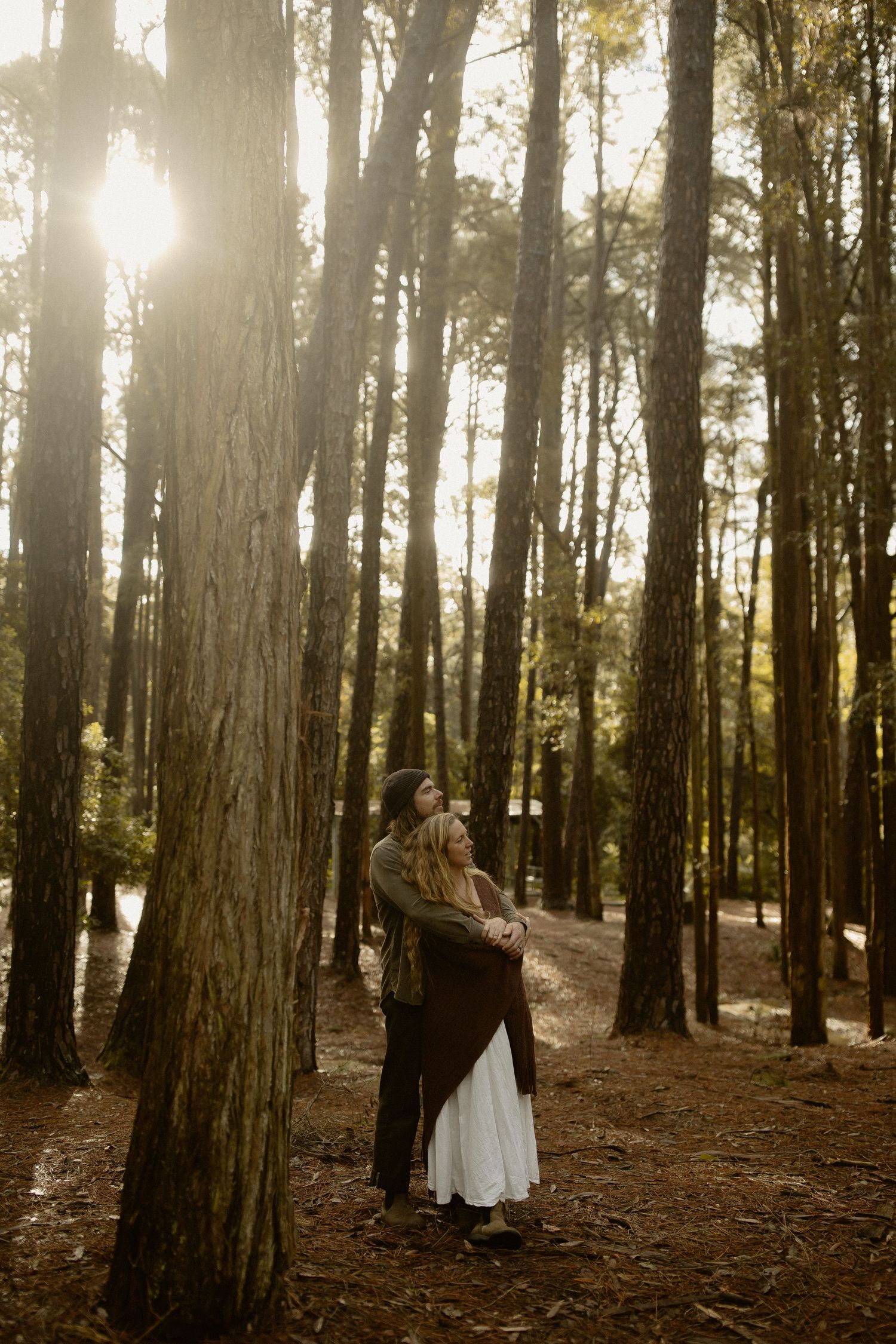 A romantic forest photography session with sunlight streaming through tall trees in a wooded setting.
