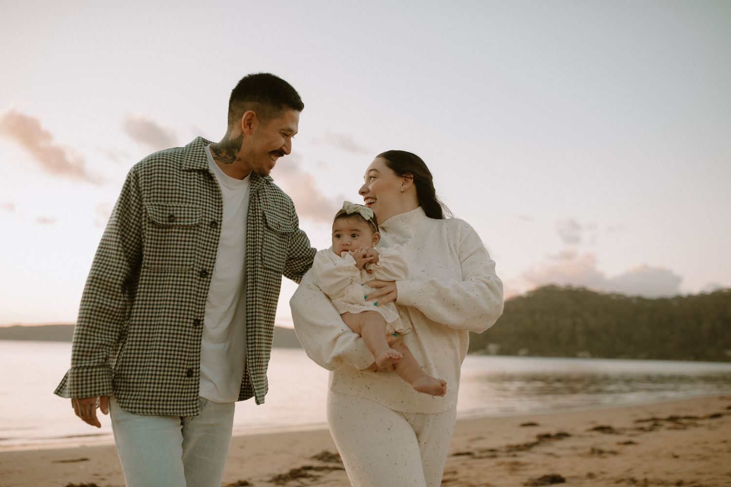 A family enjoying sunset together on a beach wearing neutral tones while holding their young child.