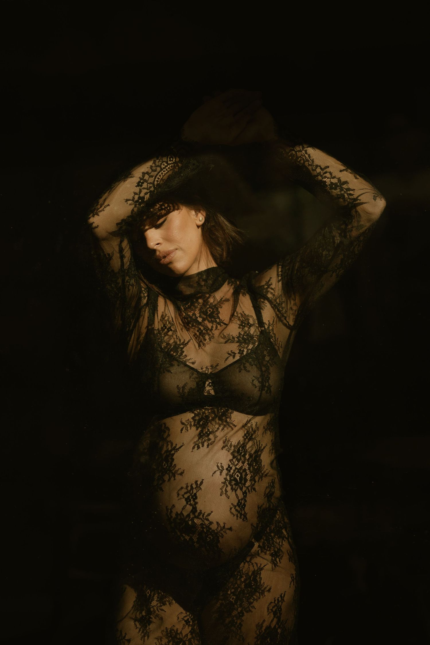 Artistic boudoir photograph featuring a figure in black lace against a dark background in moody lighting.