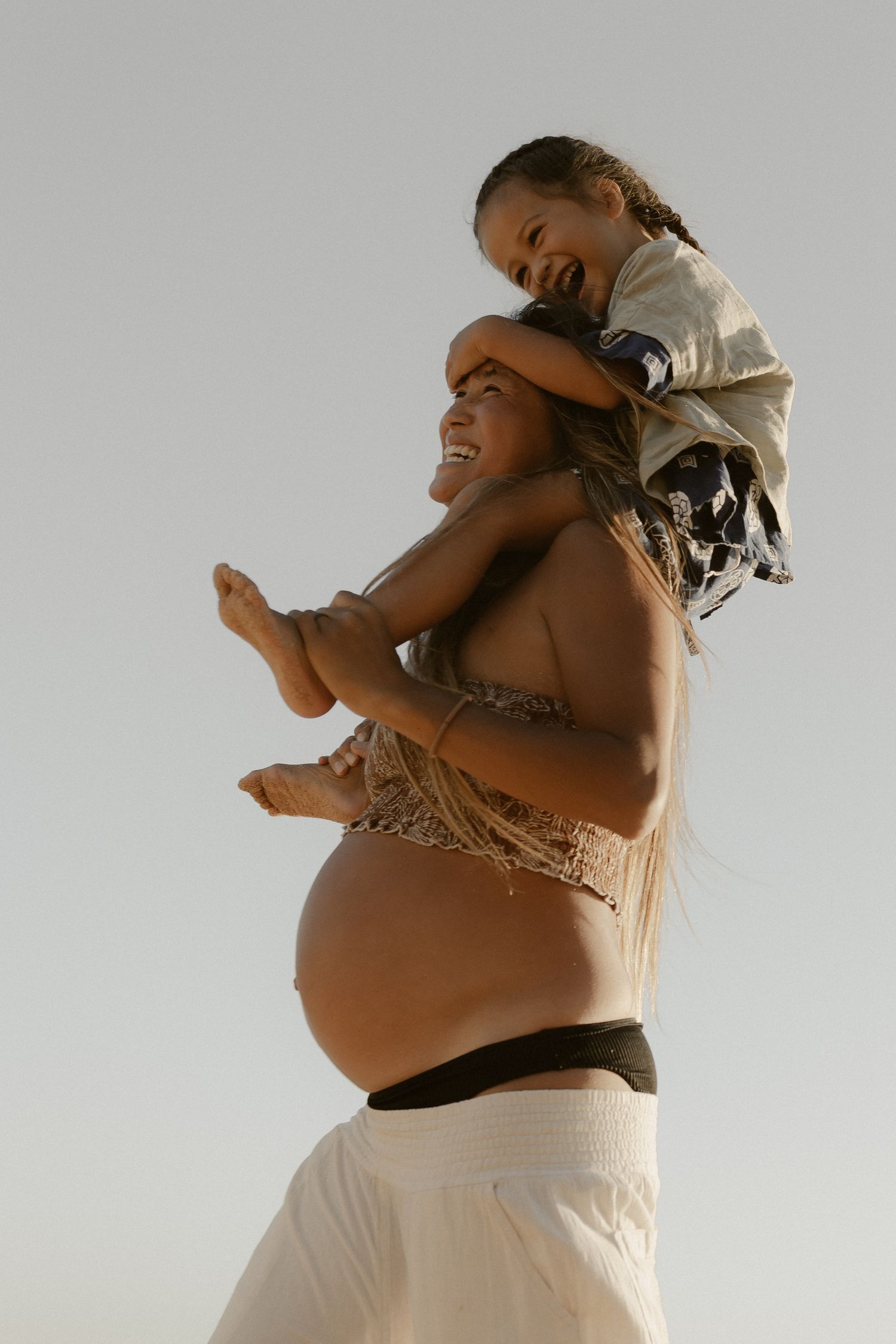A pregnant woman in white clothing twirls and dances with joy against a light background.
