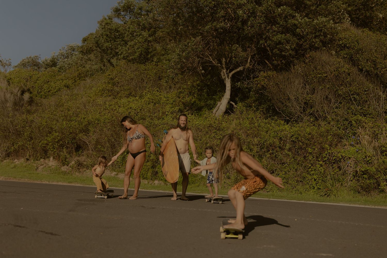 Group skateboarding down a scenic coastal road during golden hour.