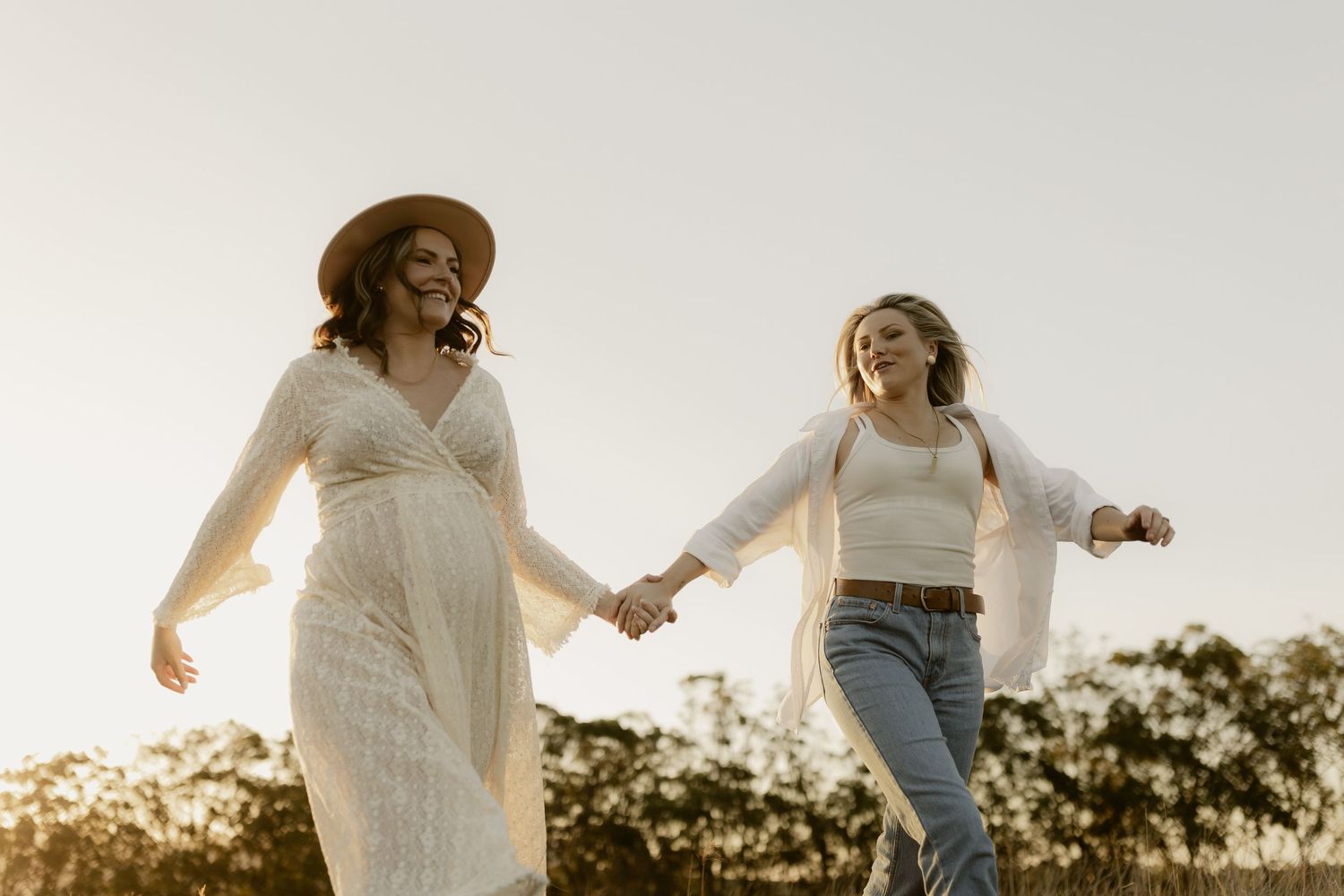 Two friends holding hands and dancing joyfully in a field during golden hour.