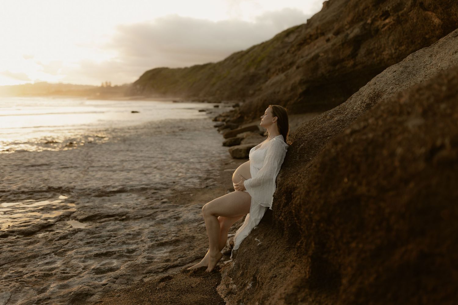 A romantic couple walks along a scenic beach at sunset with cliffs and waves creating a dreamy coastal atmosphere.