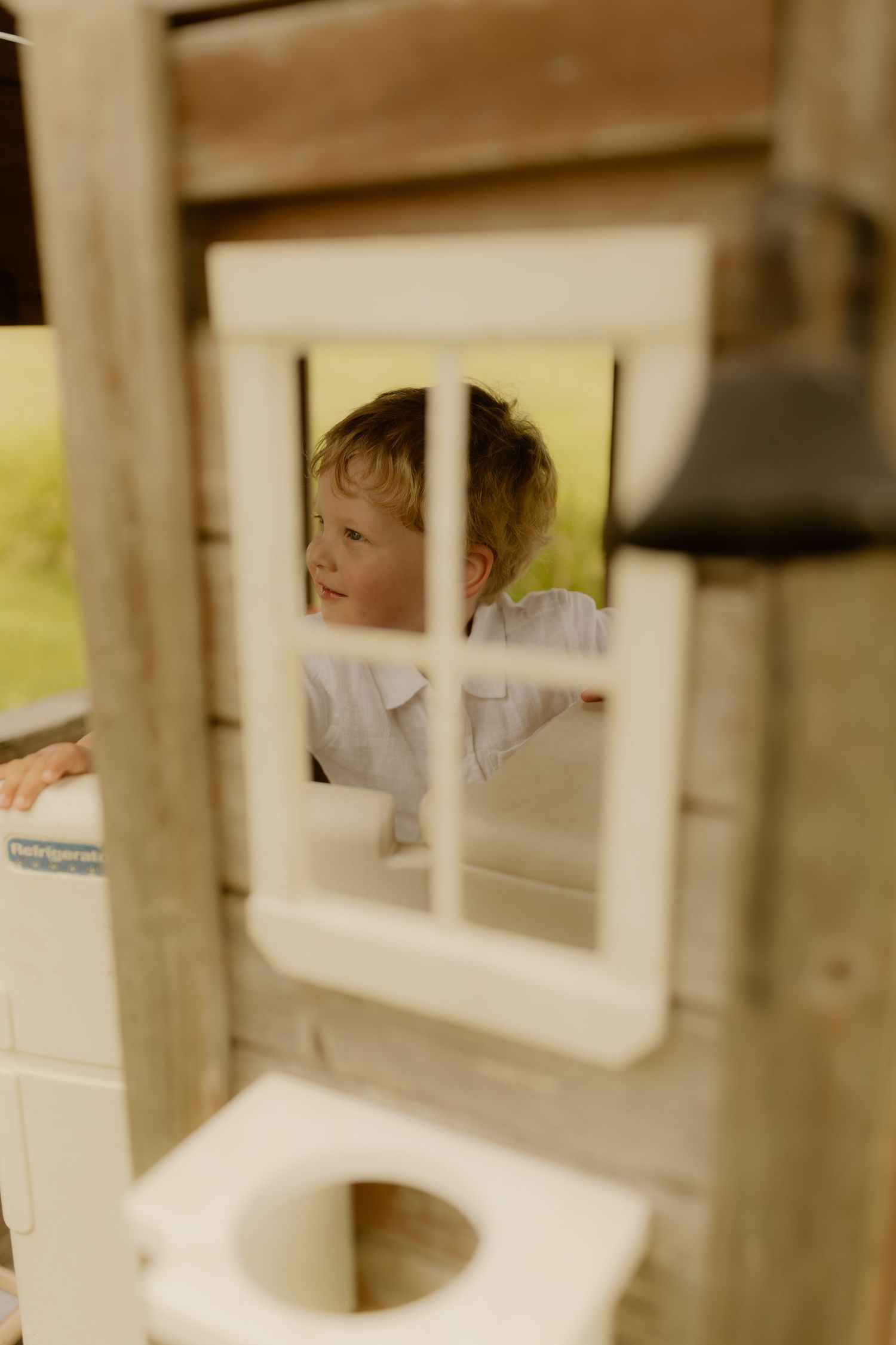 A playful peek through a white wooden window frame shows a joyful moment captured in soft focus.