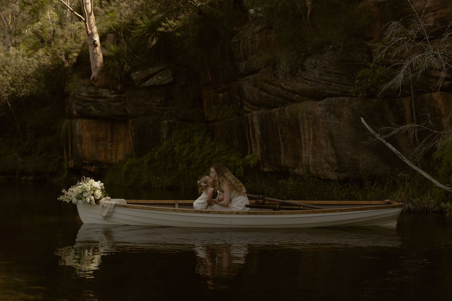 A wooden canoe glides across calm waters surrounded by lush forest reflections at dusk.