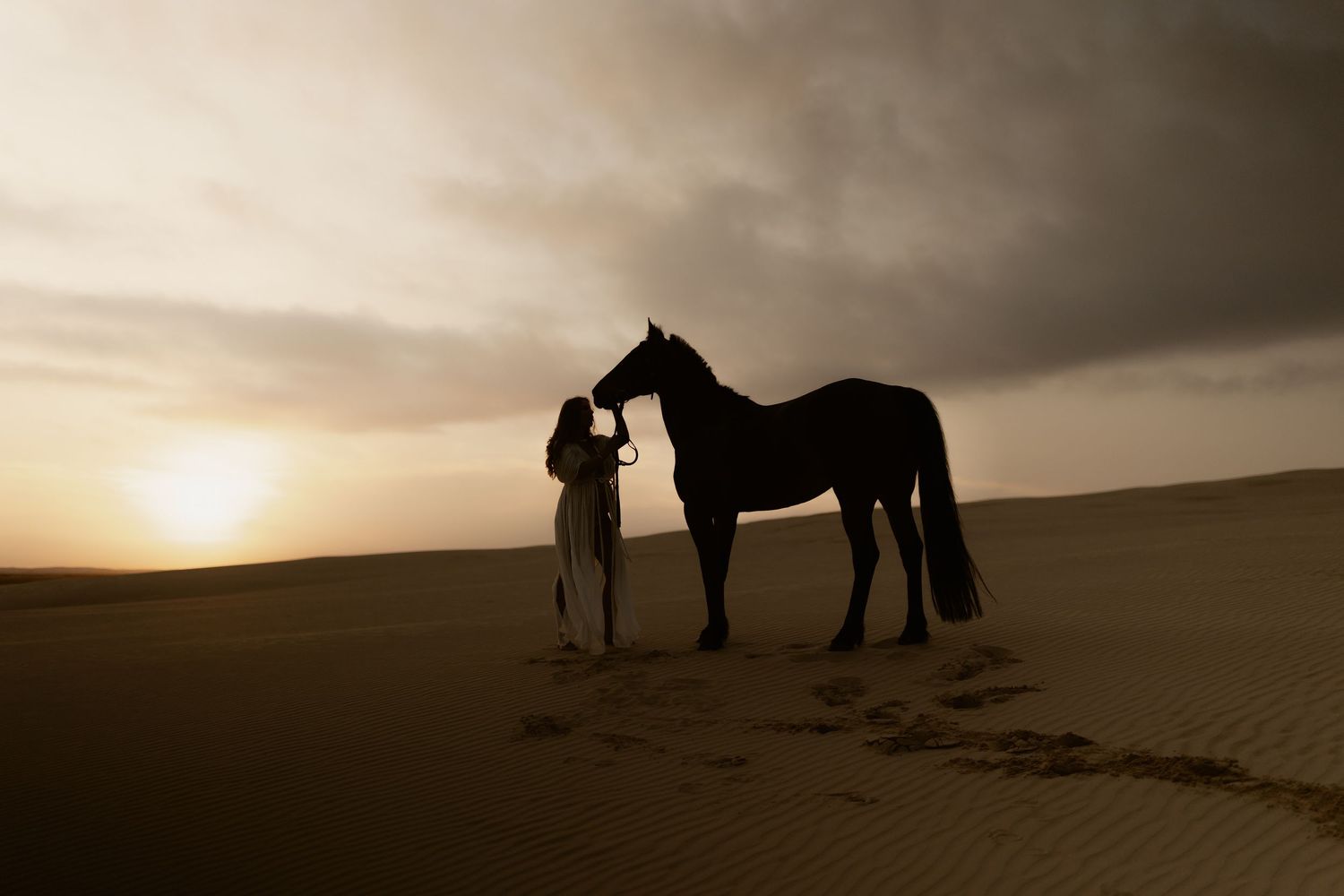 Silhouettes of horses and people against moody desert sunset creating dramatic panoramic scene.