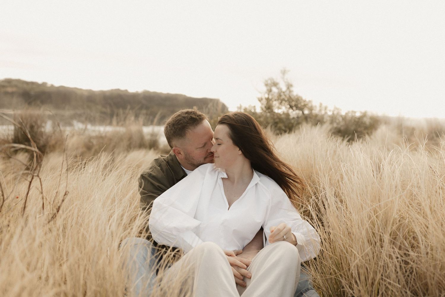 Romantic couple in white outfits embracing in a golden wheat field at sunset.