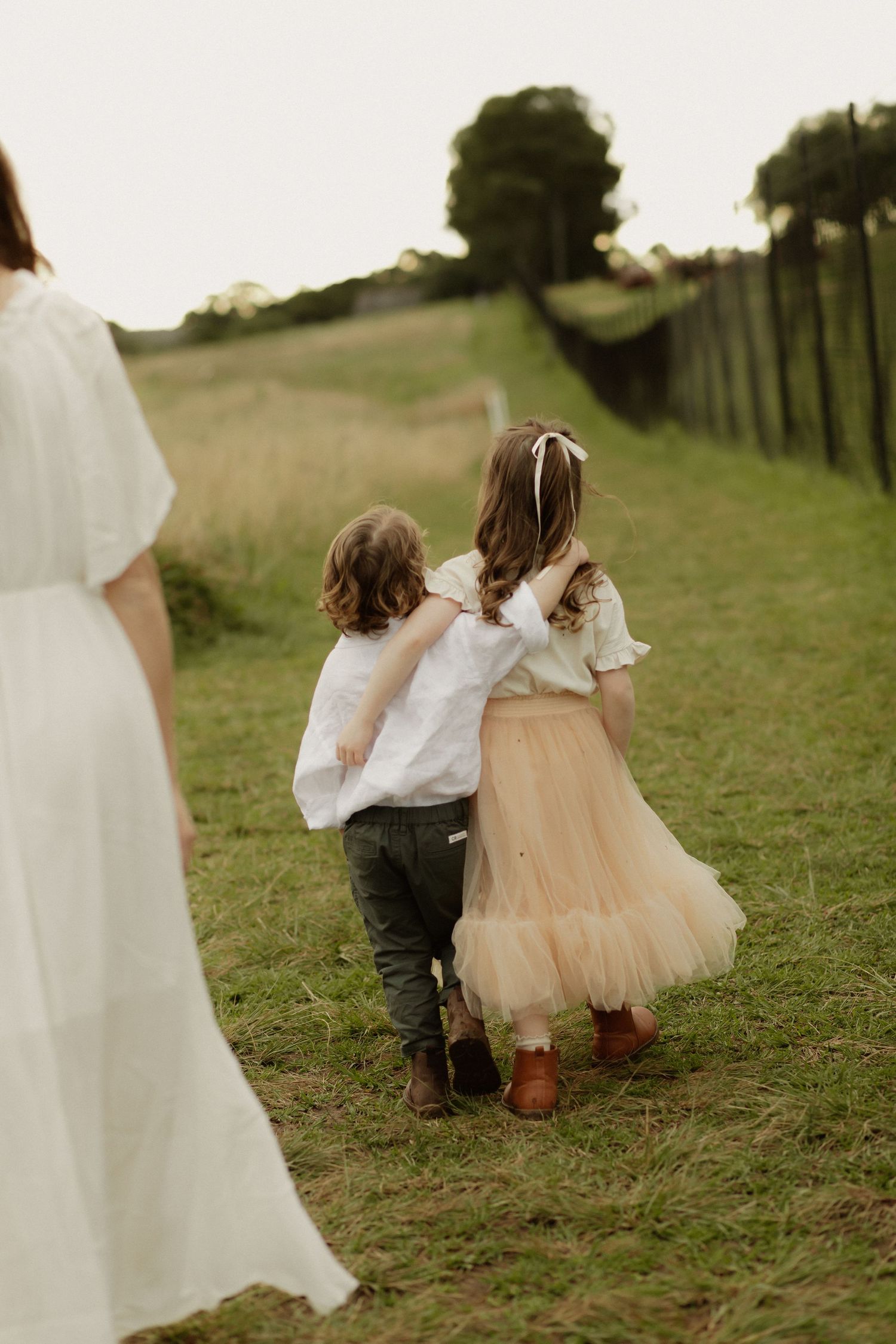 Two children walking hand in hand down a grassy path, one wearing white and the other in a tulle skirt.