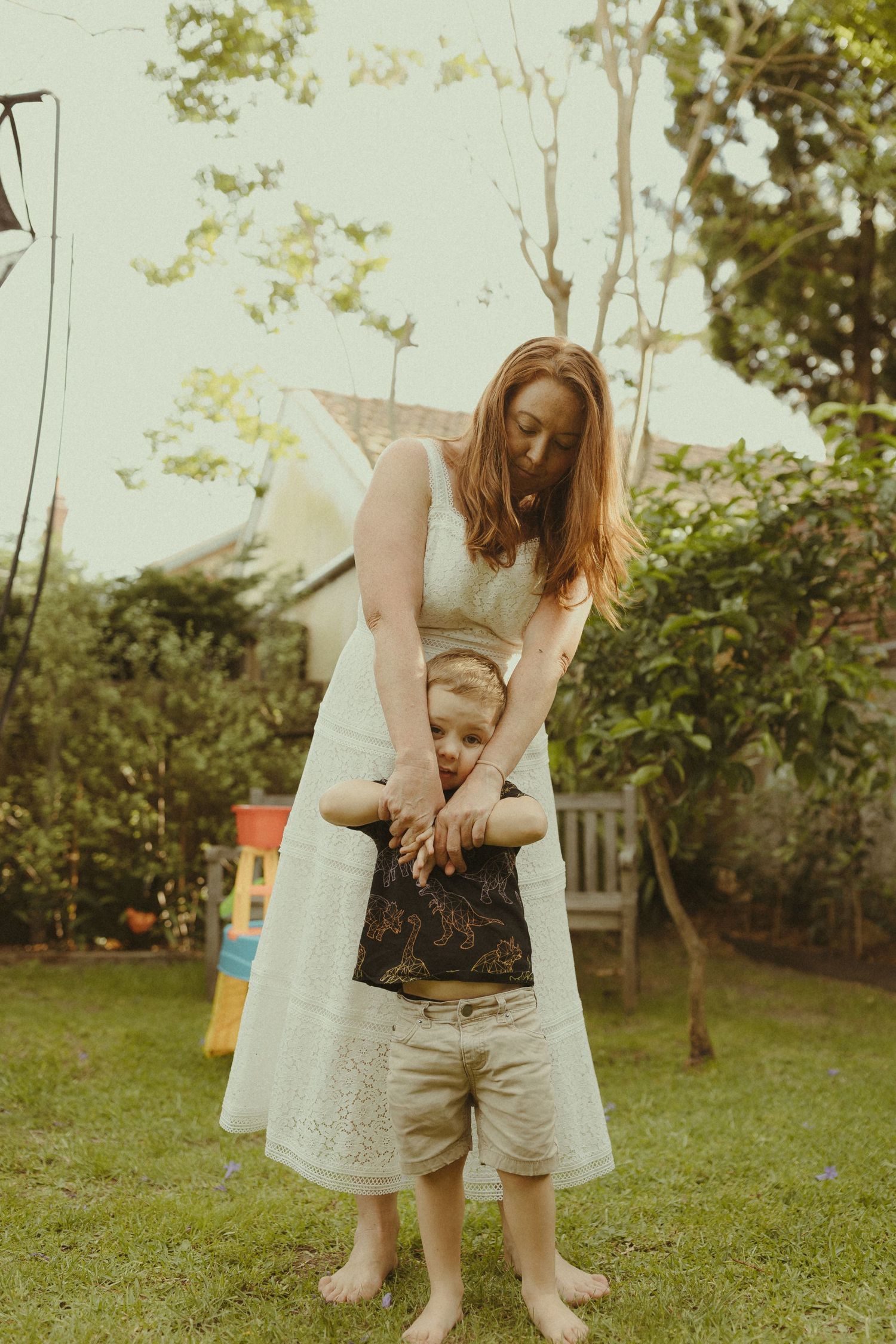 Parent and child playing together on grass in a sunlit garden setting.